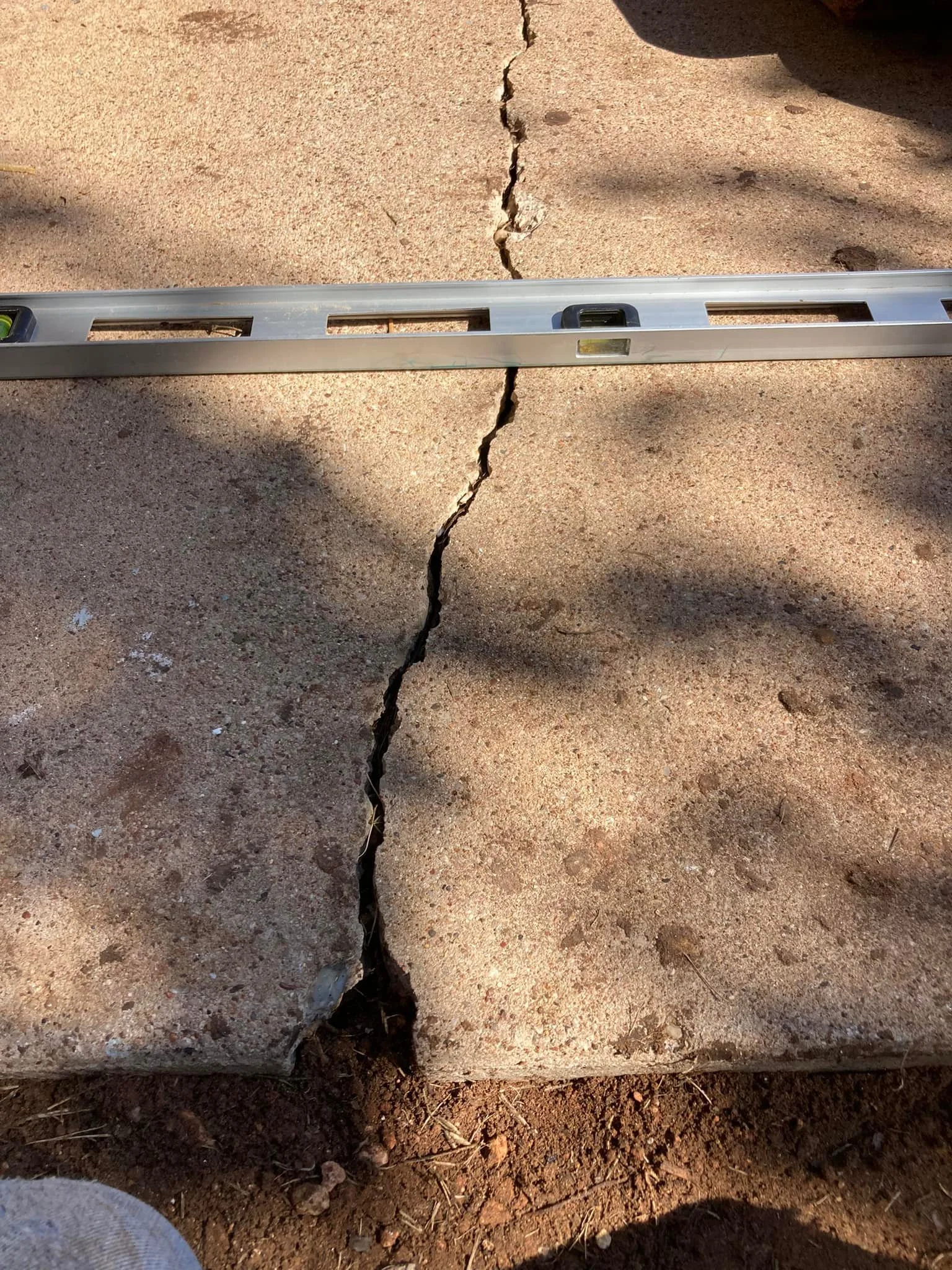 A spirit level lying on a cracked concrete sidewalk.