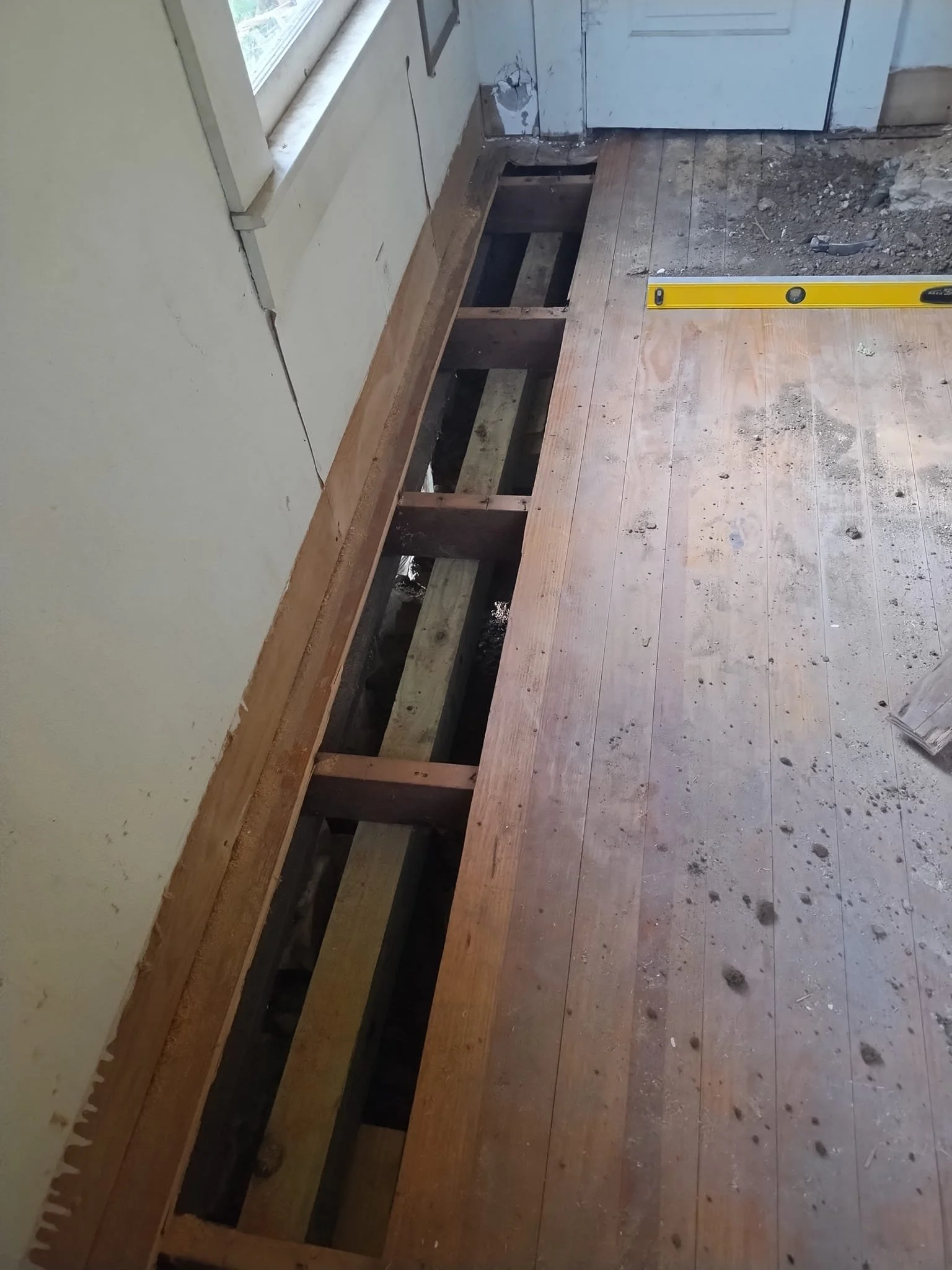Room floor under construction with exposed wooden joists and a level tool on the floor.