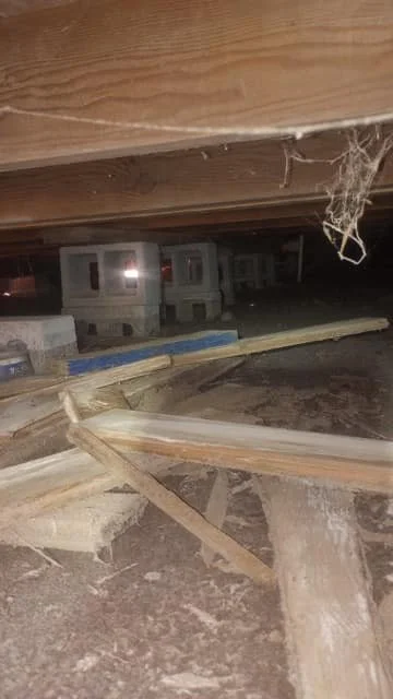 View of debris and construction materials under a wooden structure at night, with partially built concrete blocks in the background.