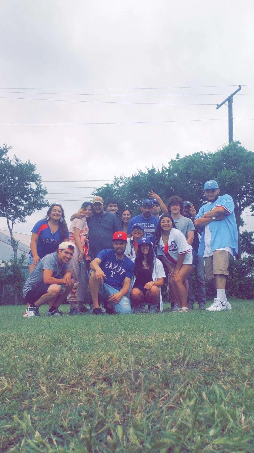 Group of people outdoors on a grassy field, some wearing Texas Longhorns or Dallas Cowboys apparel, posing for a photo on a cloudy day.