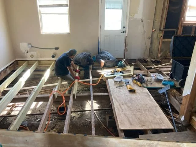 Workers renovating and installing floor joists in a room with construction tools and materials.