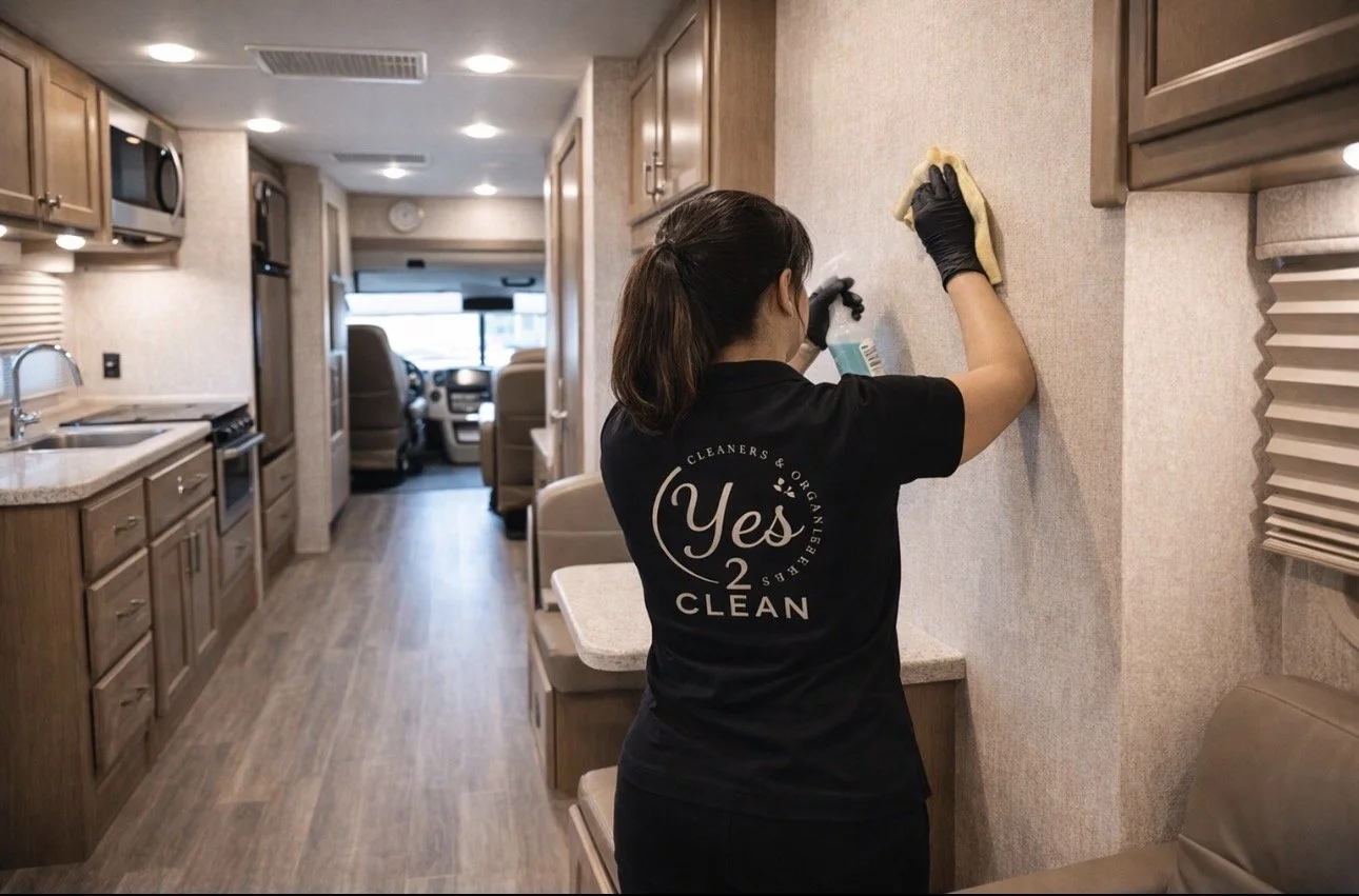 A woman cleaning the wall of an RV interior with a cloth and spray bottle.