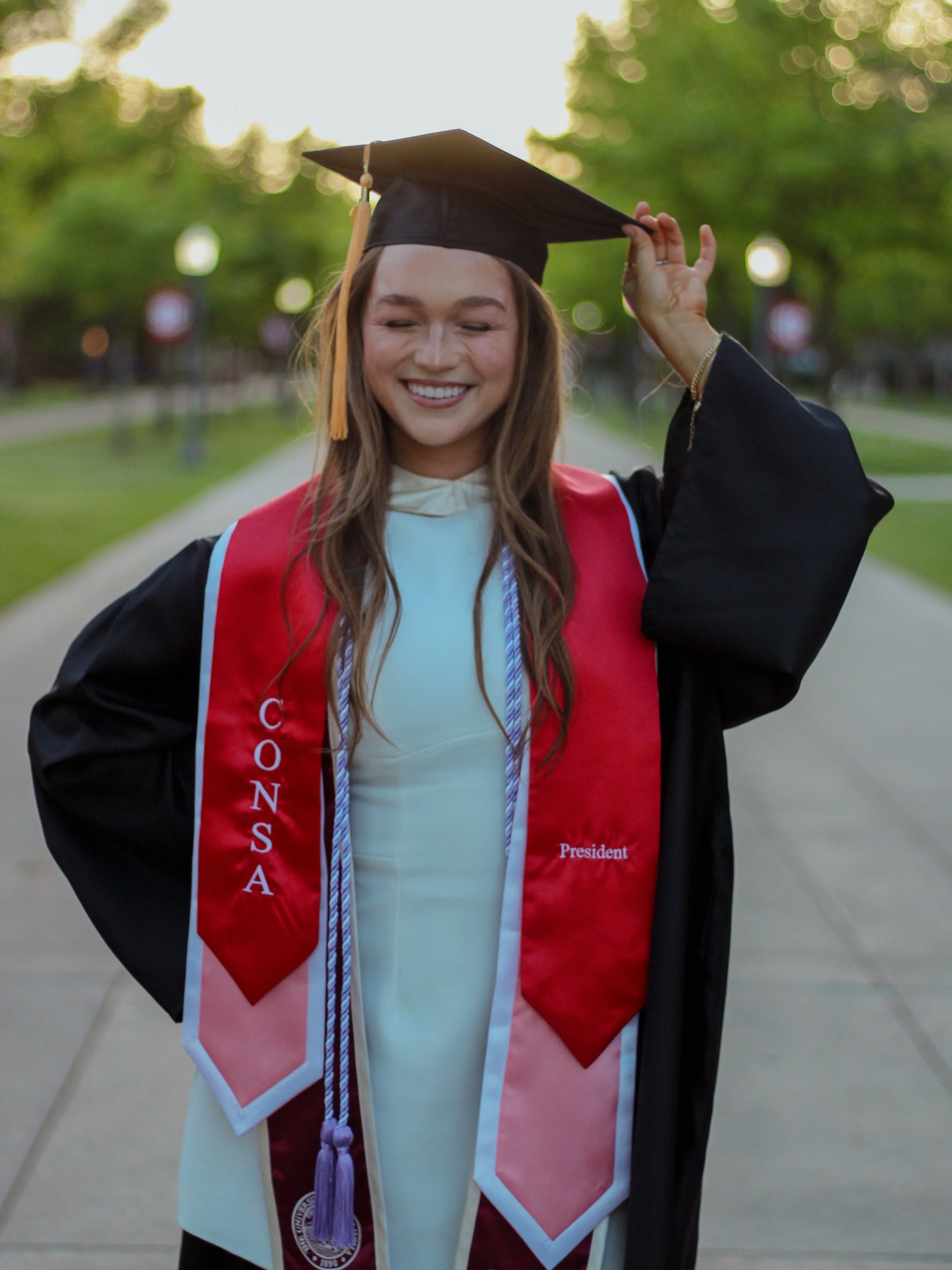 A female OU College grad smiling and holding her cap