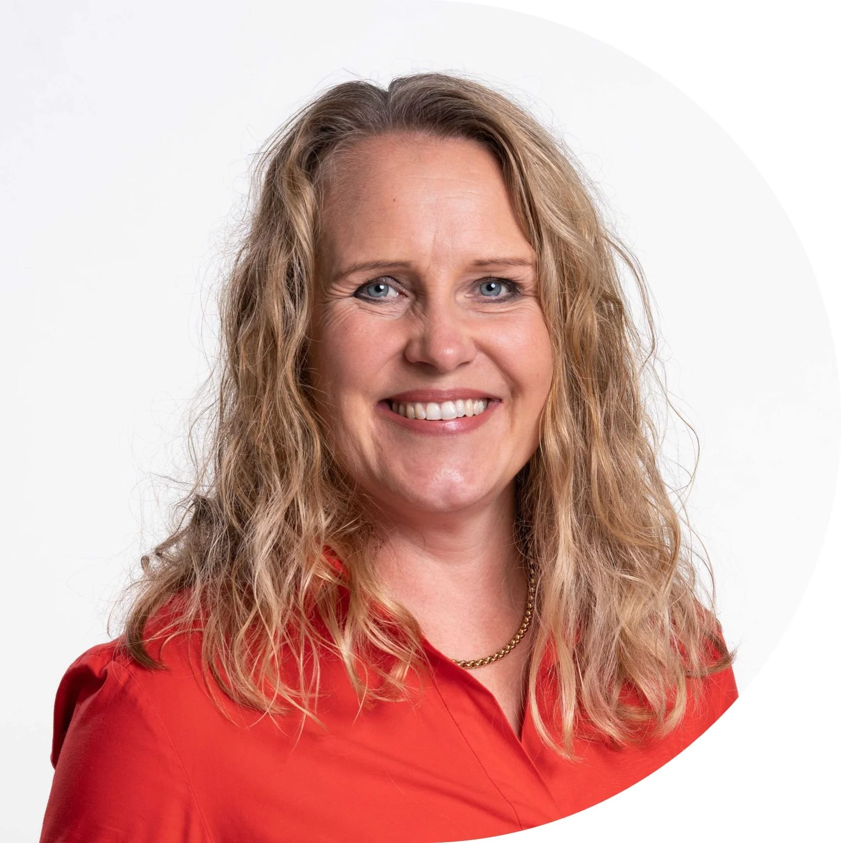 smiling woman with wavy blonde hair wearing a red blouse and gold necklace