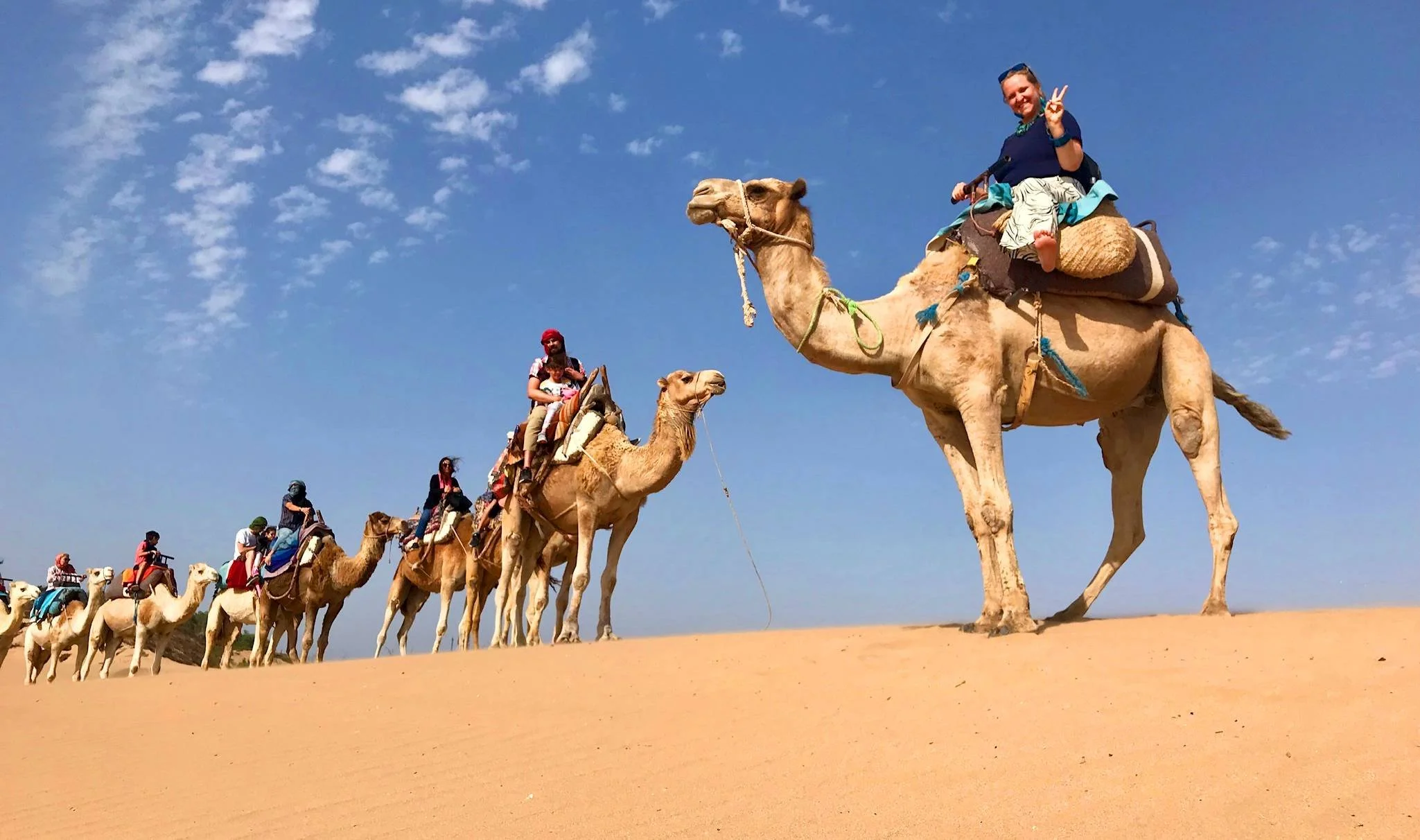 Tourists riding camels in a desert under a clear blue sky.