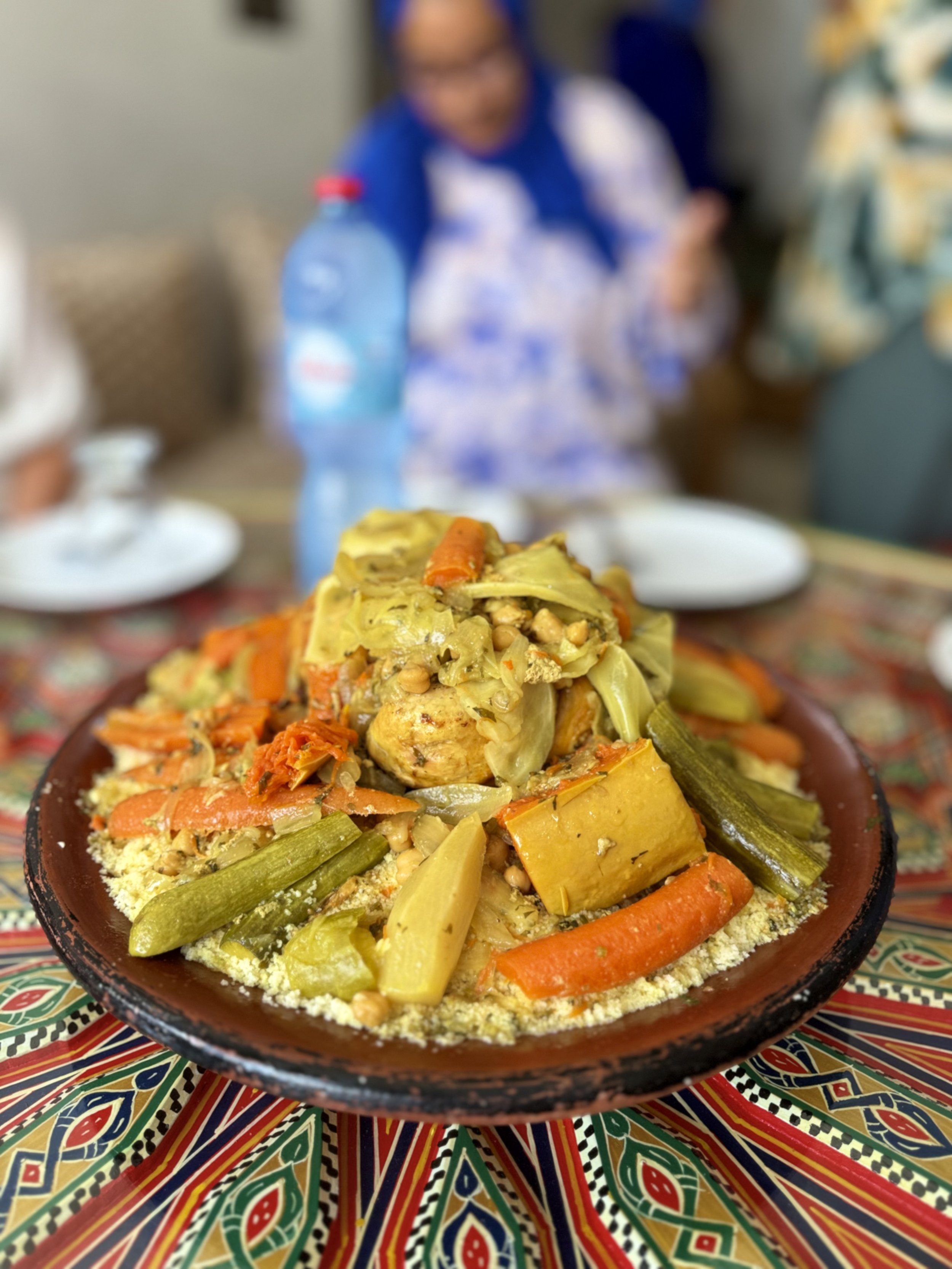 A colorful plate of Mexican food with vegetables and grains, placed on a traditional patterned tablecloth, blurred in the background