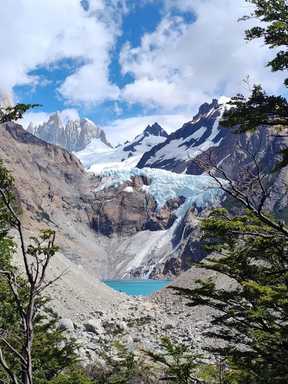 A glacier in a mountainous region with snow-covered peaks under a clear blue sky.
