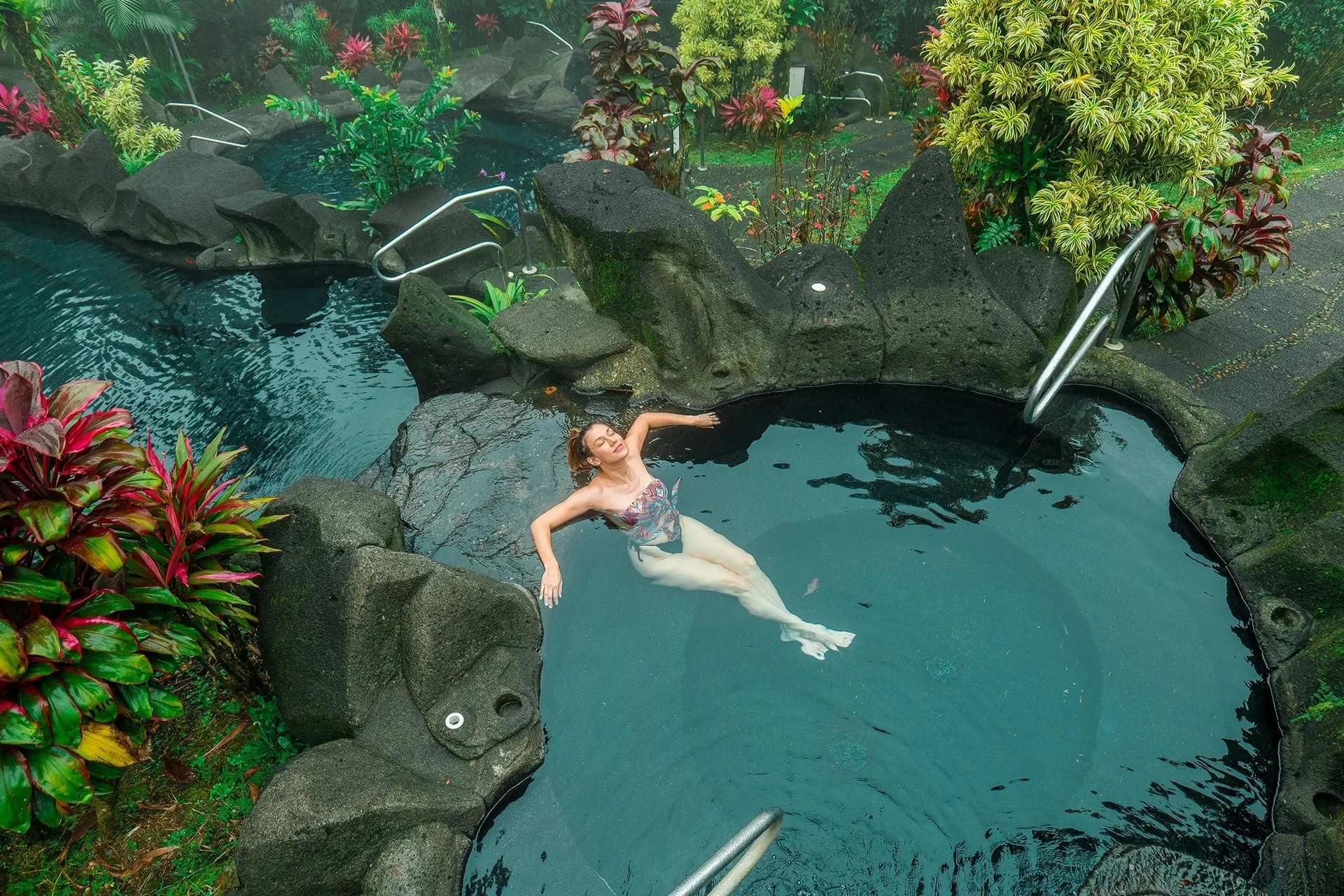 A woman with gray hair sitting in a boat on turquoise water, watching another boat pass by with mountains in the background under a bright blue sky.