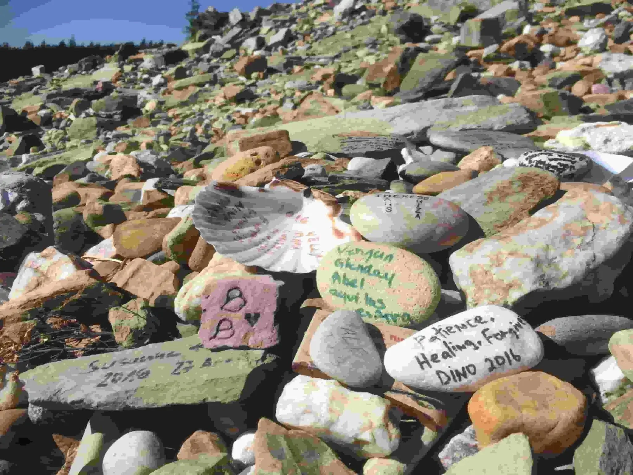 Colorful painted rocks with handwritten messages on a rocky surface outdoors.