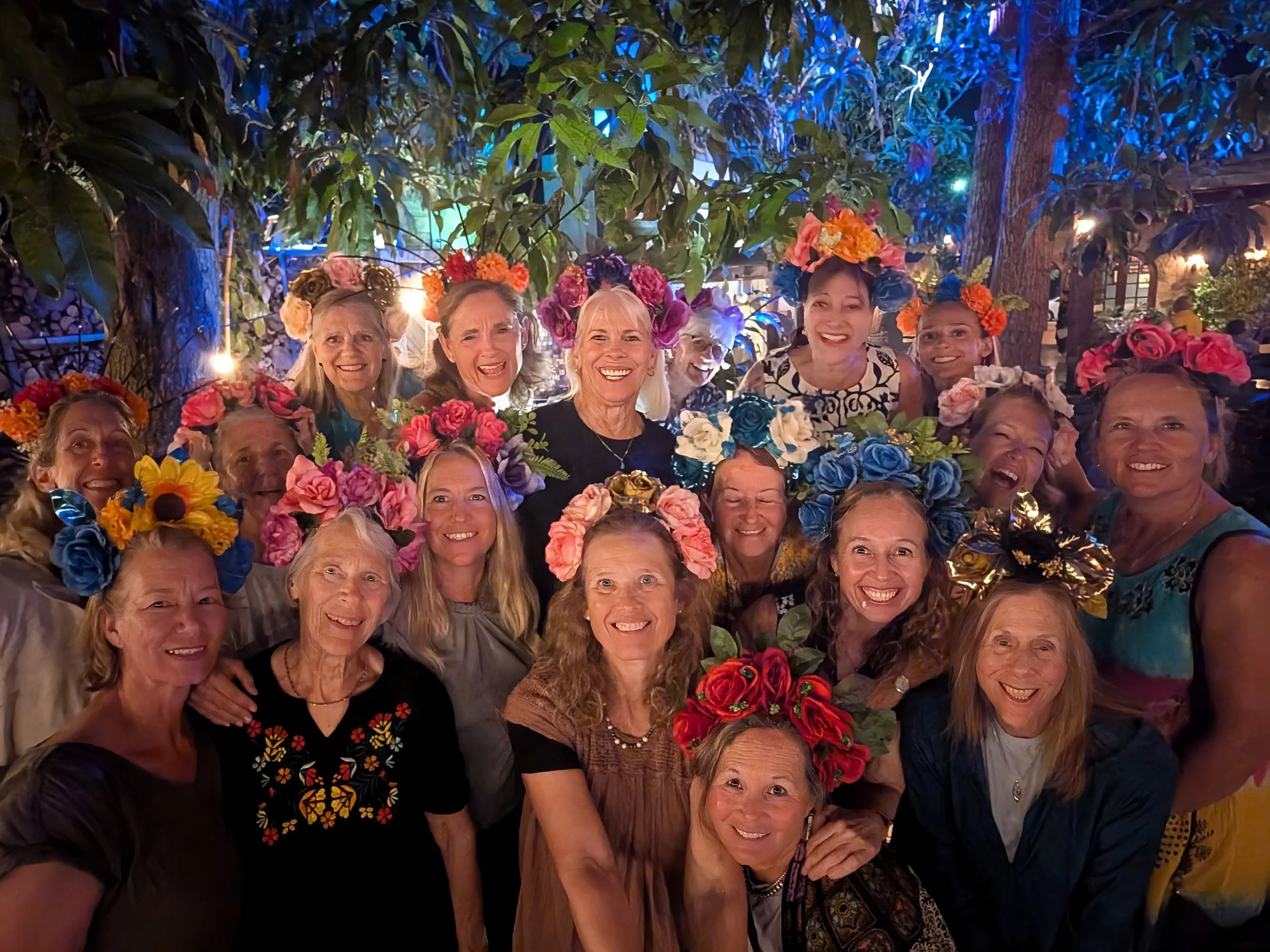 A group of women wearing colorful flower crowns posing in a garden at night.