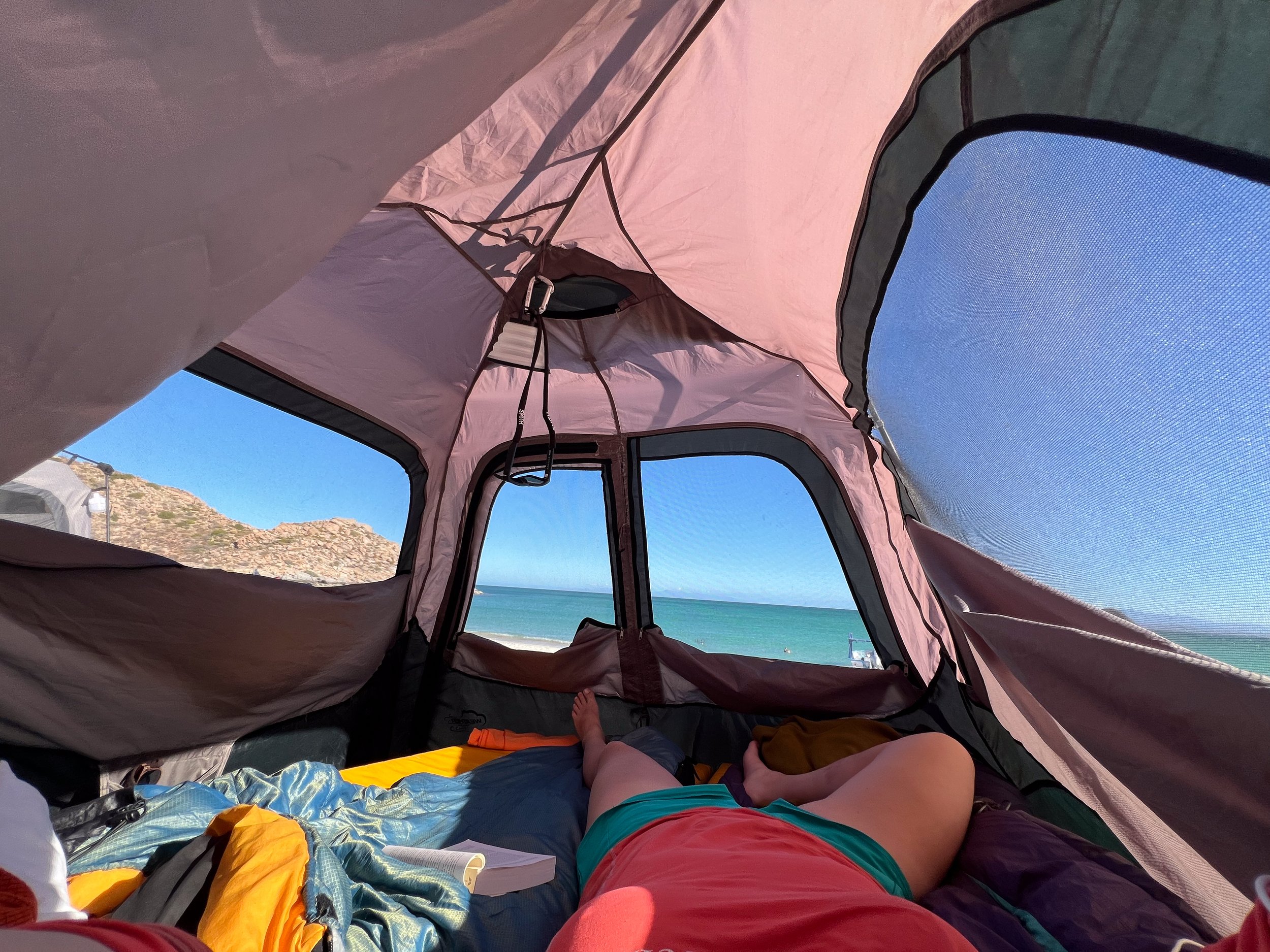 Inside a beach tent showing a person lying down in front of the ocean view with mountains in the background.