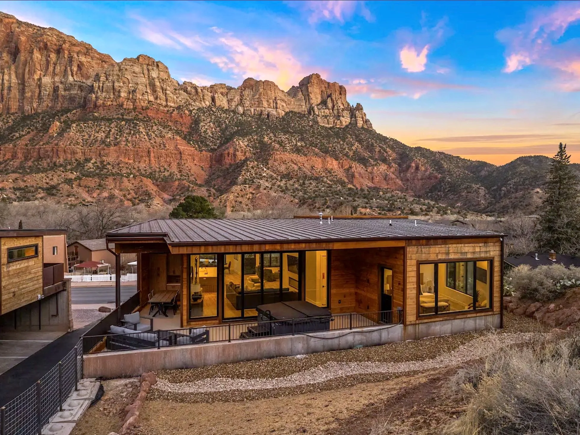Modern house with large glass windows and doors, with mountains and a colorful sky in the background.
