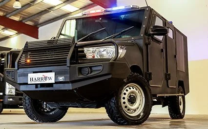 Black armored police or security vehicle with blue emergency lights on top, parked indoors.