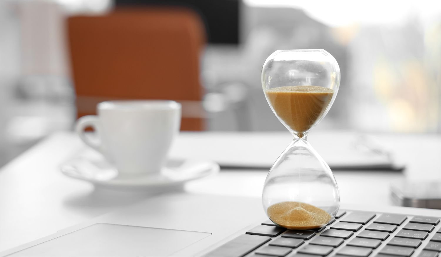 An hourglass on an executive office desk representing the limited time companies have to hire top sales and marketing talent before candidates accept other offers.