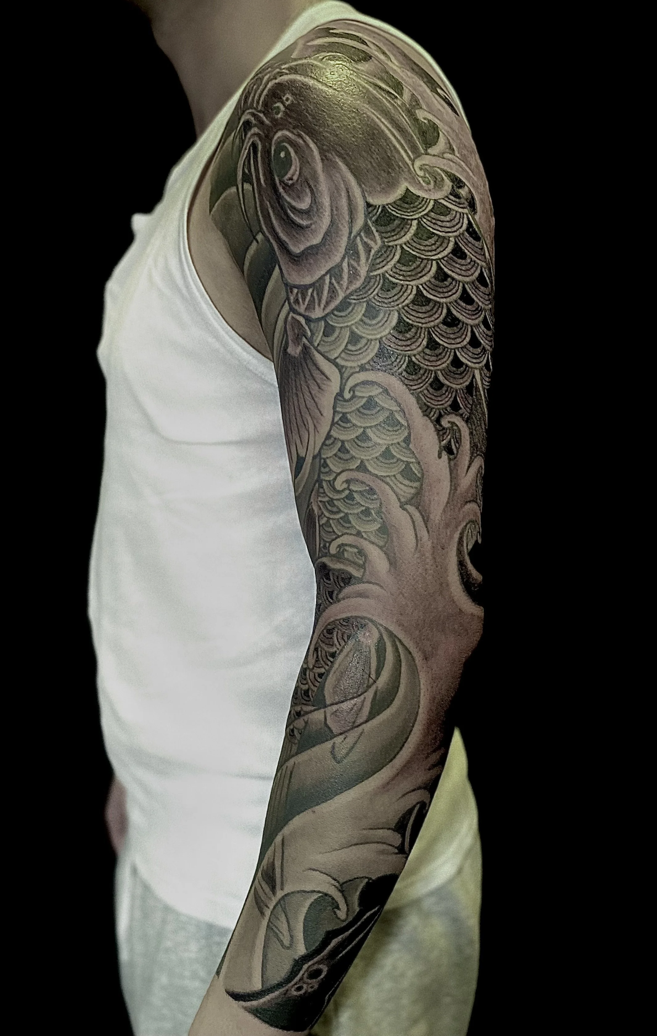 Tattoo of a fish with waves on a person's upper arm.