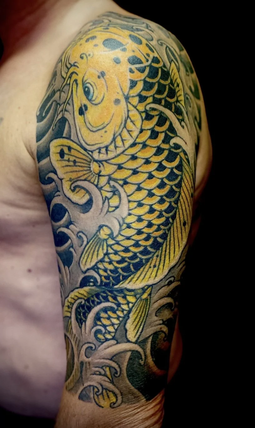 Tattoo of a fierce-looking koi fish with yellow and black scales, surrounded by stylized waves, inked on a person's upper arm and shoulder.