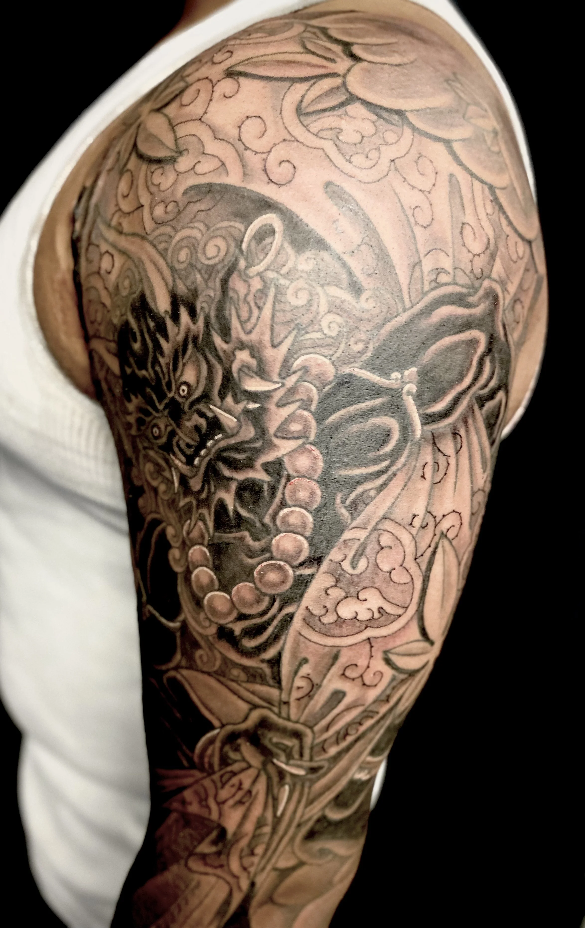 Tattoo of a fierce dragon with sharp claws and detailed scales, incorporating traditional Japanese art elements with clouds and waves, covering the person's upper arm and shoulder.