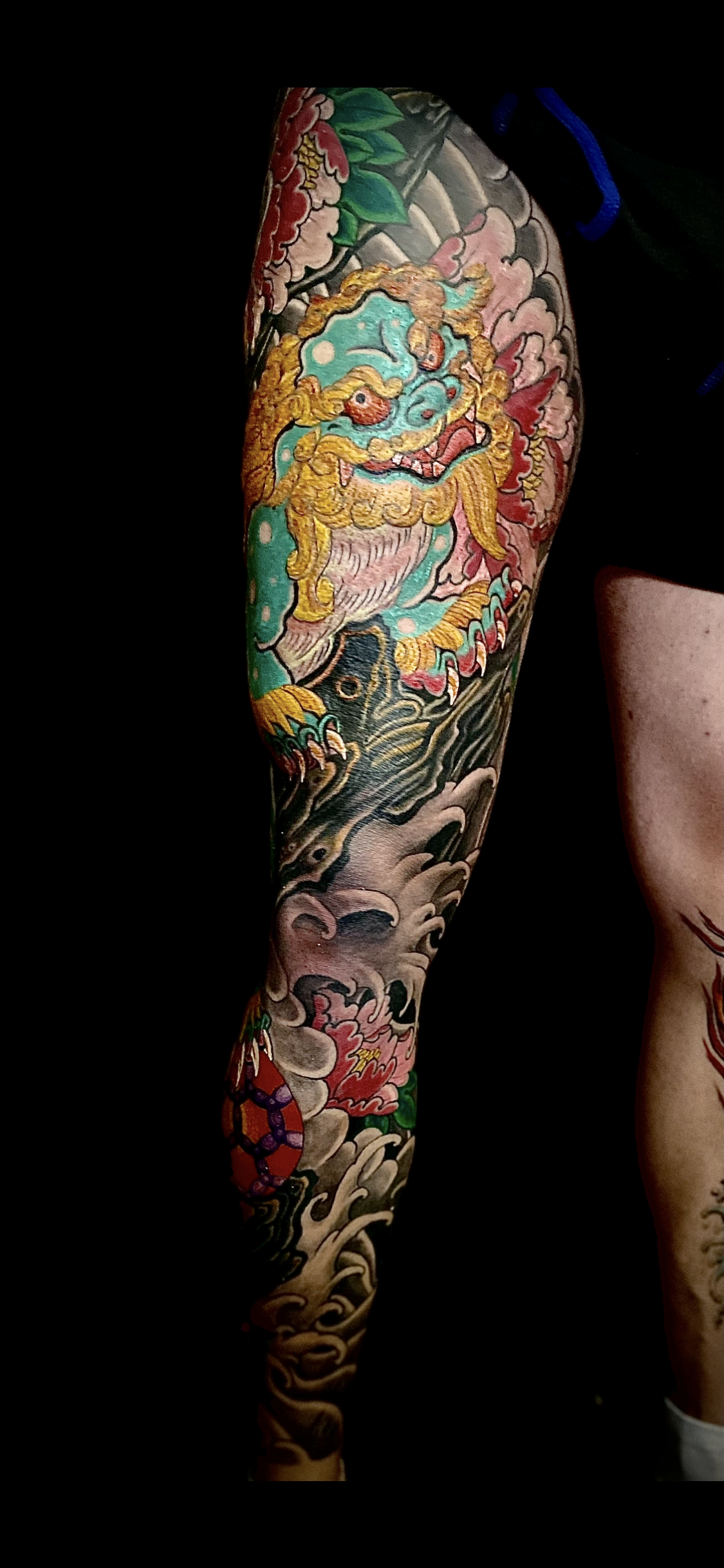 Colorful tattoo featuring a fierce lion with a flowing mane, surrounded by traditional Japanese elements such as waves and floral designs.