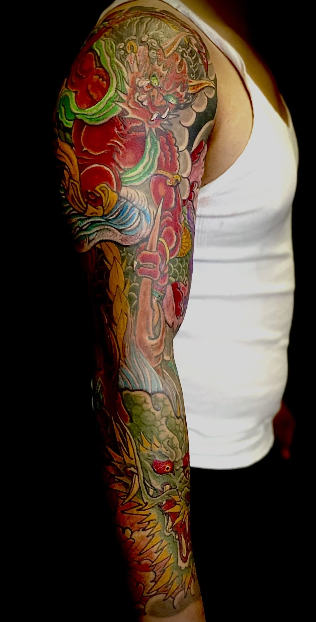 Colorful tattoo sleeve featuring a dragon, clouds, and flames on a person's arm.