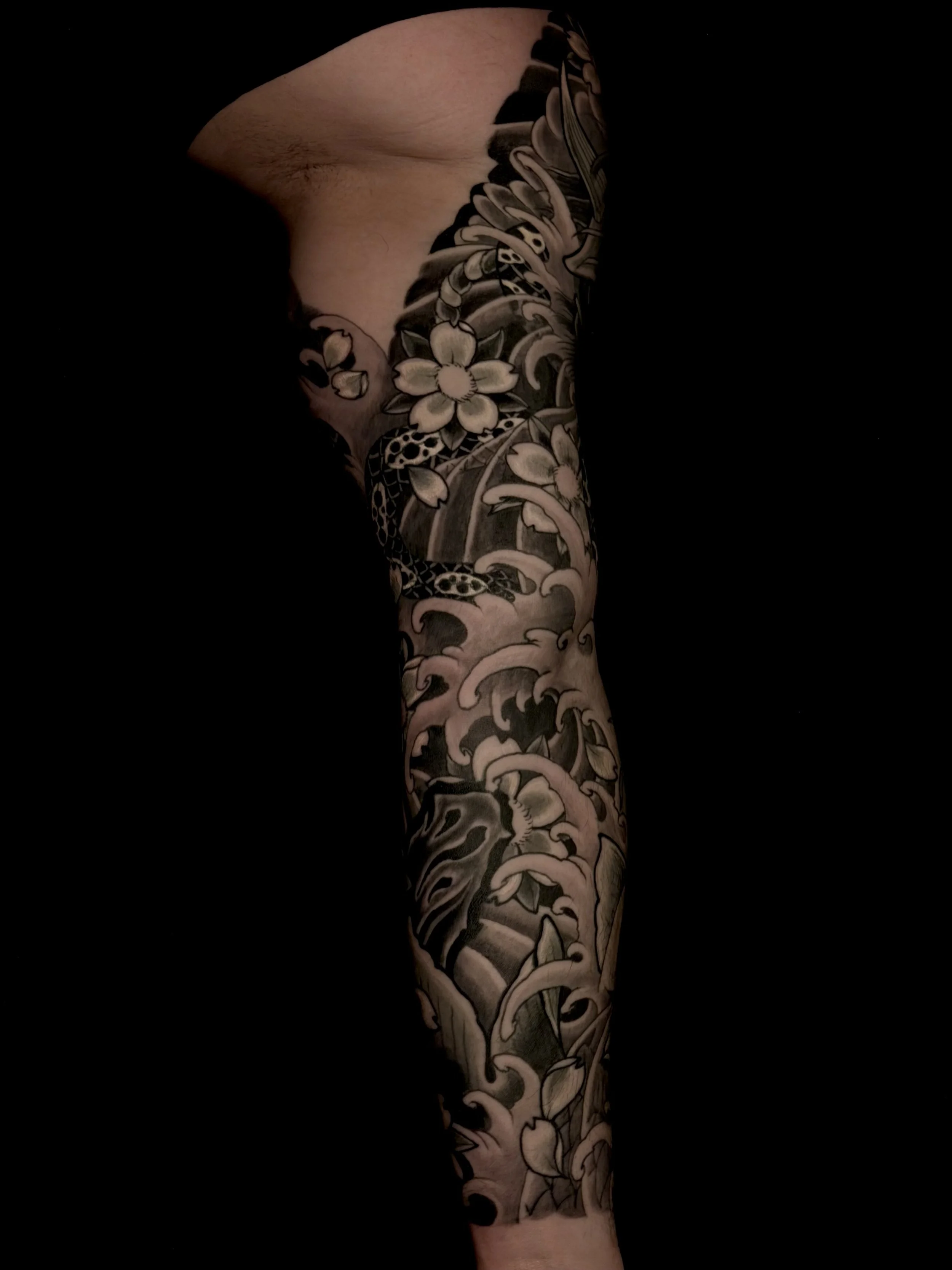 Close-up of a person's arm with a detailed black and white floral and wave tattoo sleeve.
