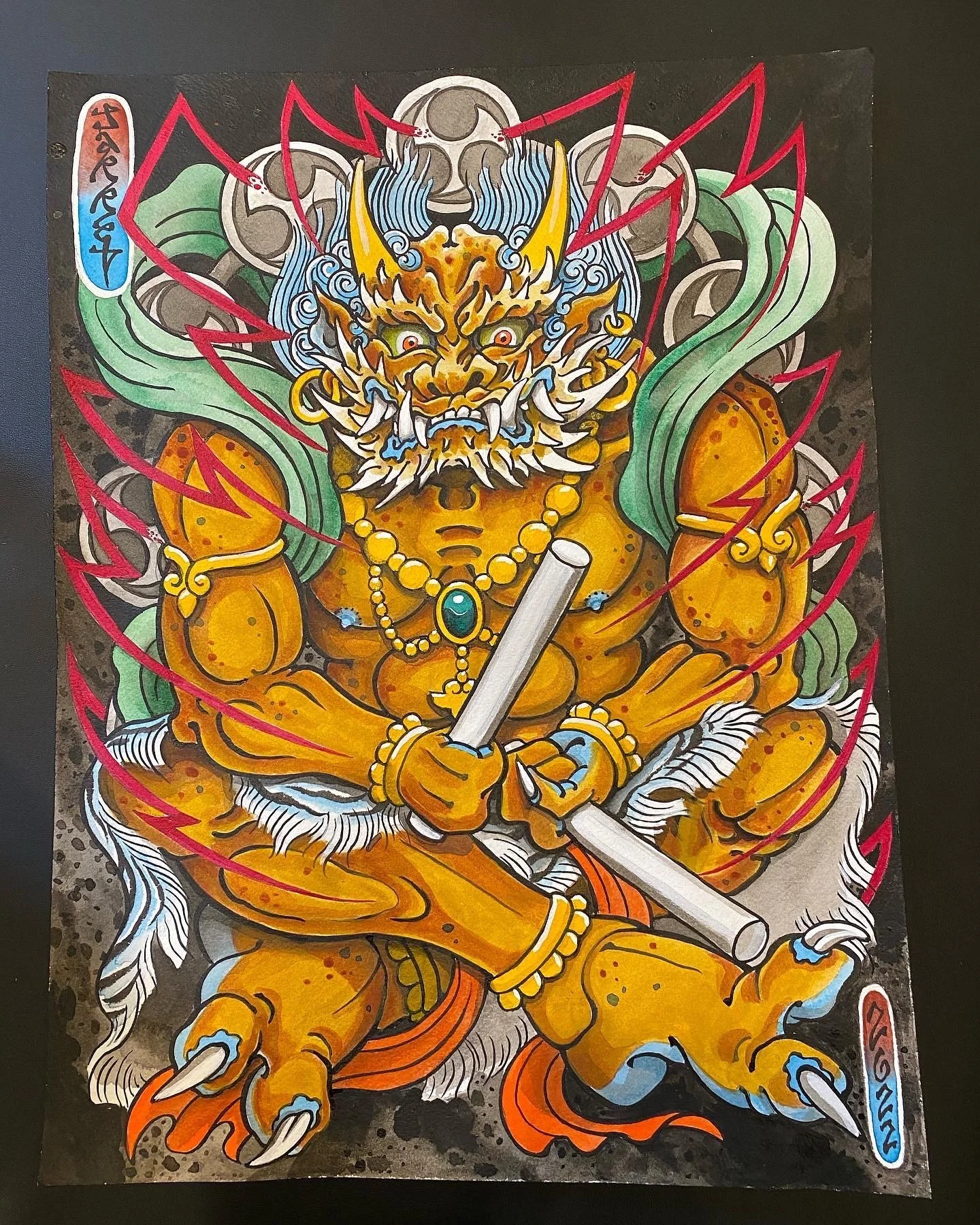 Colorful illustration of a fierce, yellow, demon-like creature with a lion's face, horns, and tusks, holding a white scroll, sitting cross-legged with red lightning around it, wearing jewelry and armor.