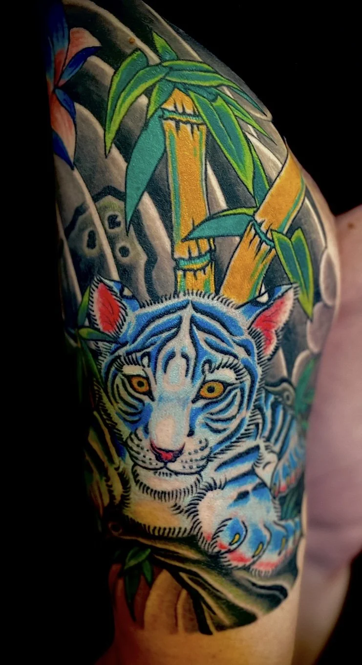 Colorful tattoo of a tiger, bamboo leaves, and bamboo stalks on a person's arm.
