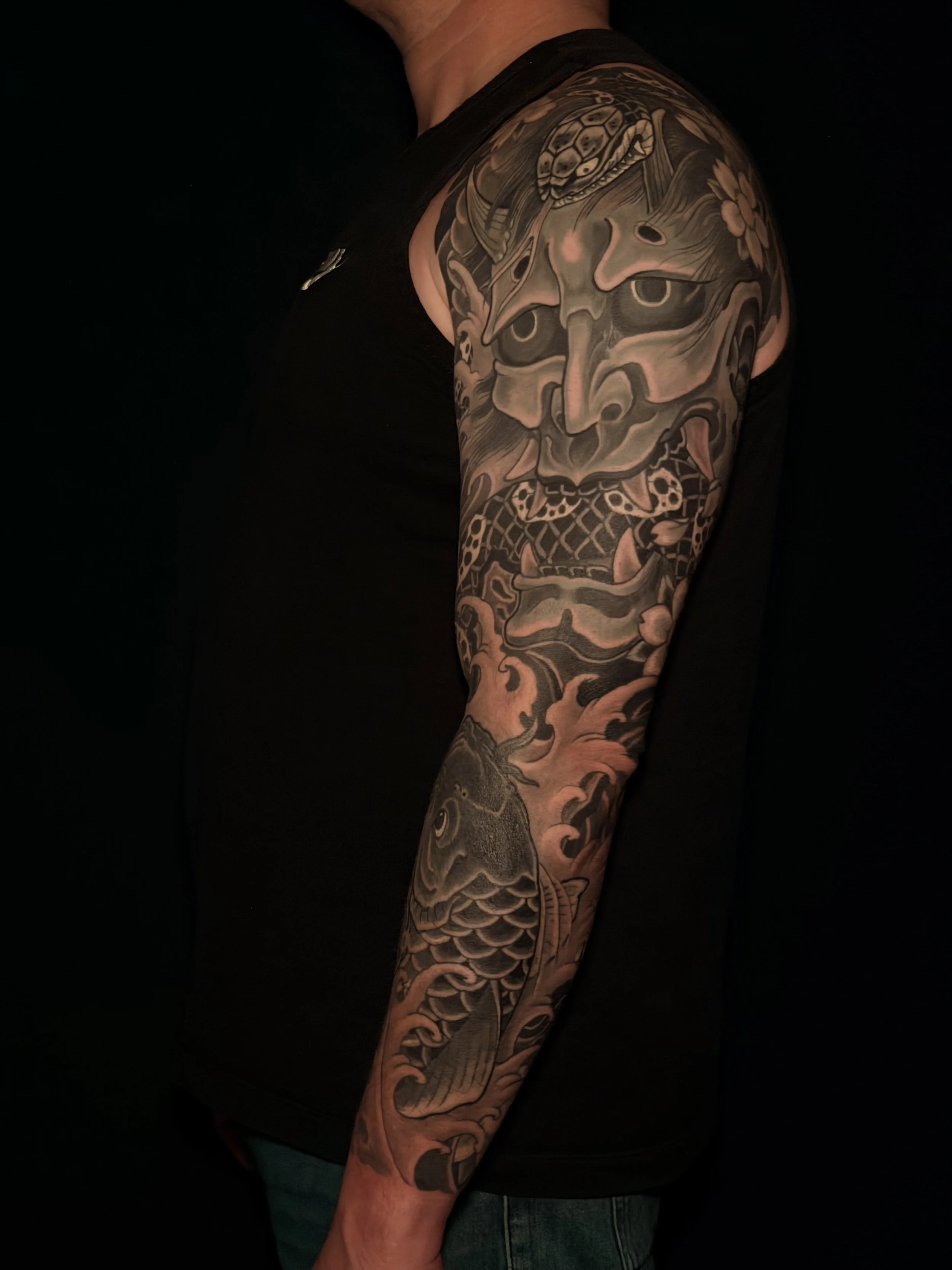 Tattooed arm with a detailed black and gray Japanese-style dragon and mask design.