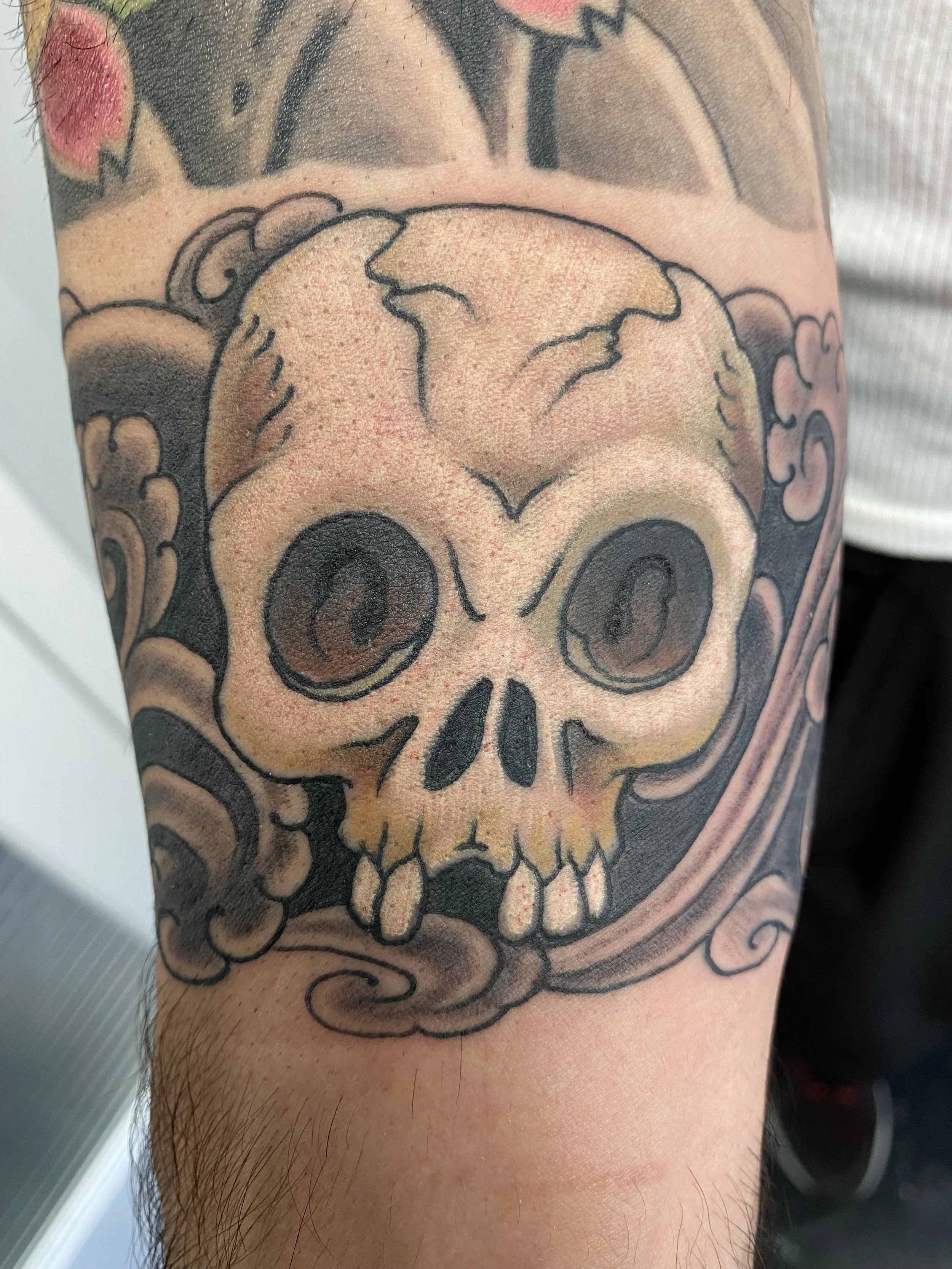 Tattoo of a skull with stylized, swirling clouds around it.