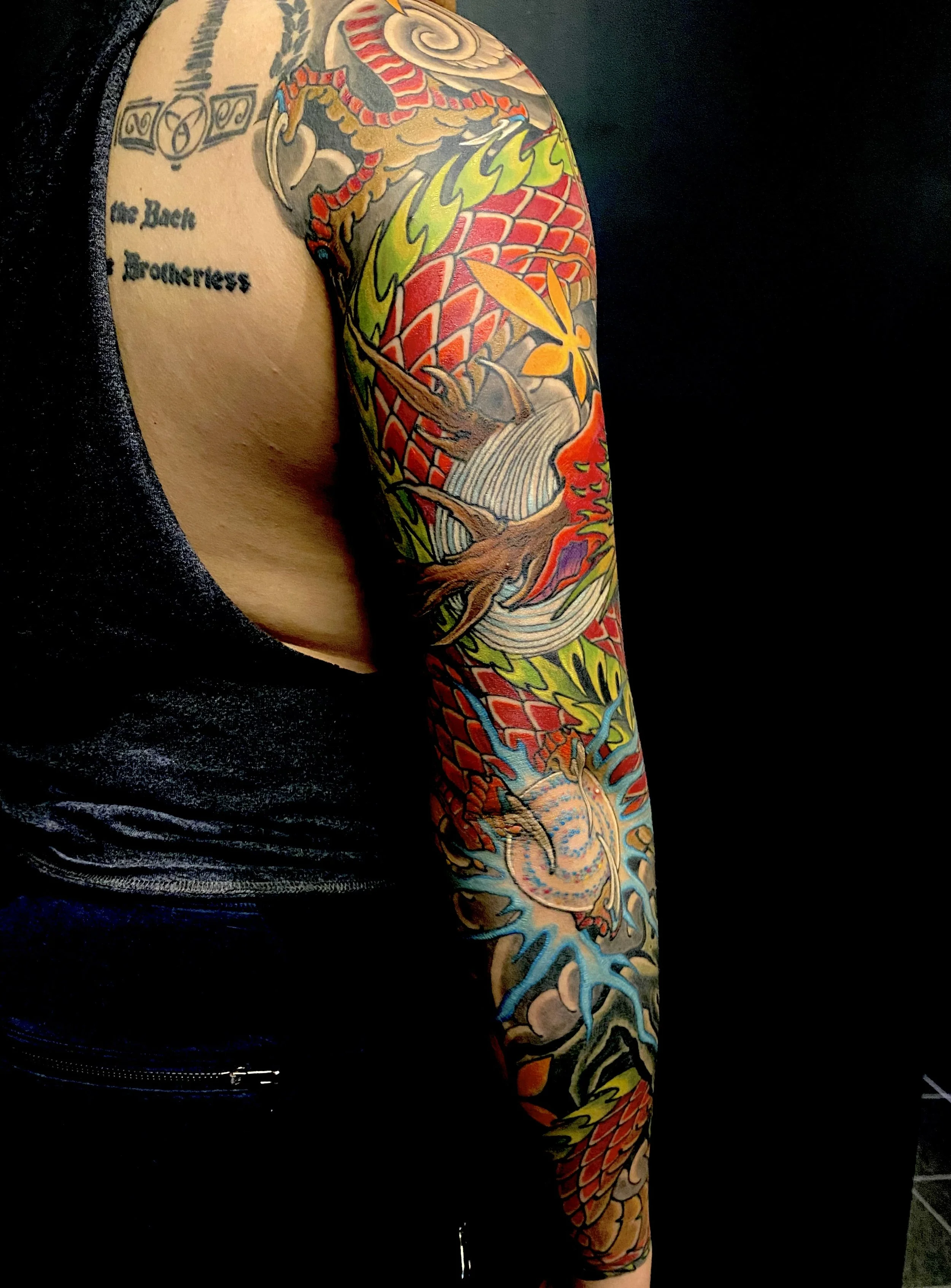 Colorful Japanese-style dragon tattoo on a person's arm, featuring a red and orange dragon with green flames, clouds, and a blue lightning bolt.