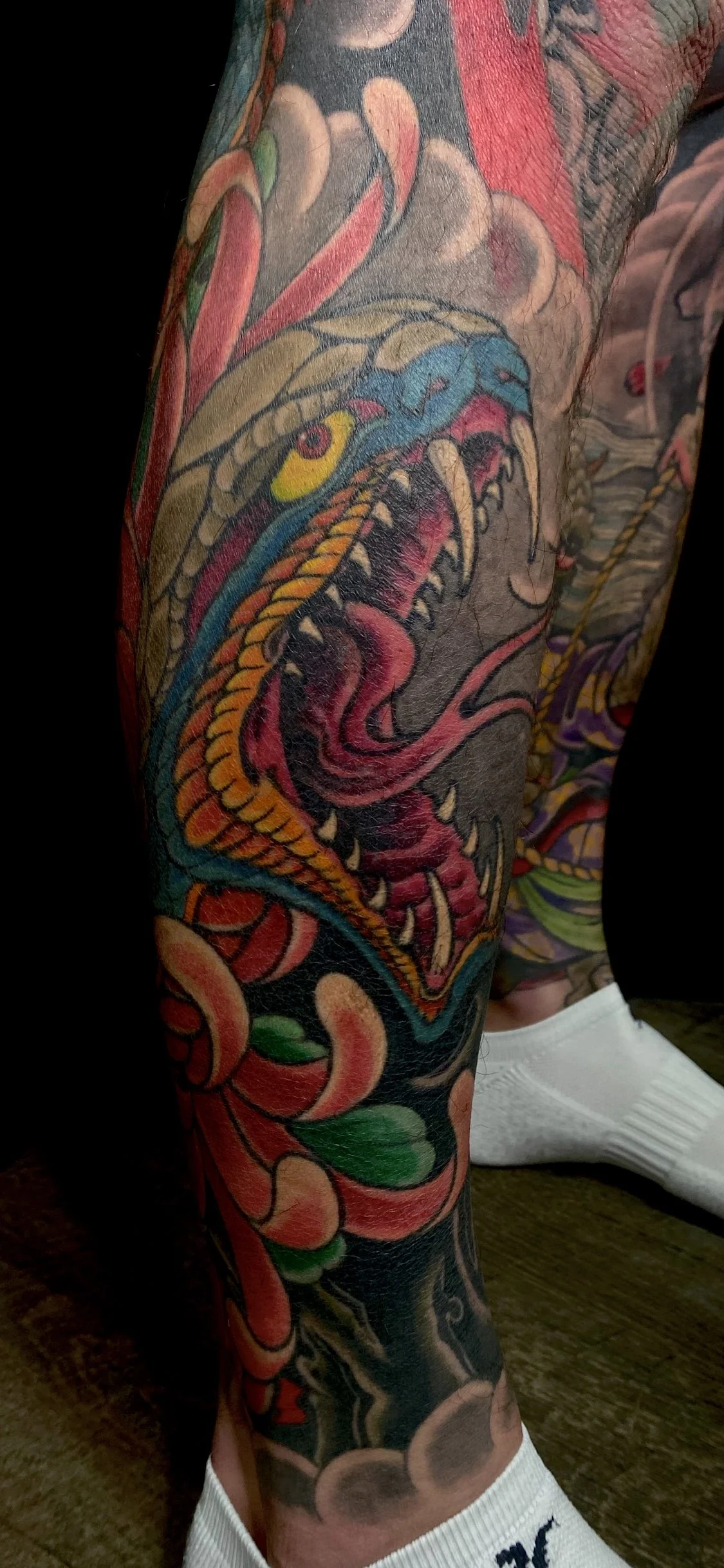 Colorful tattoo of a fierce dragon with sharp teeth and vivid colors covering the person's leg.