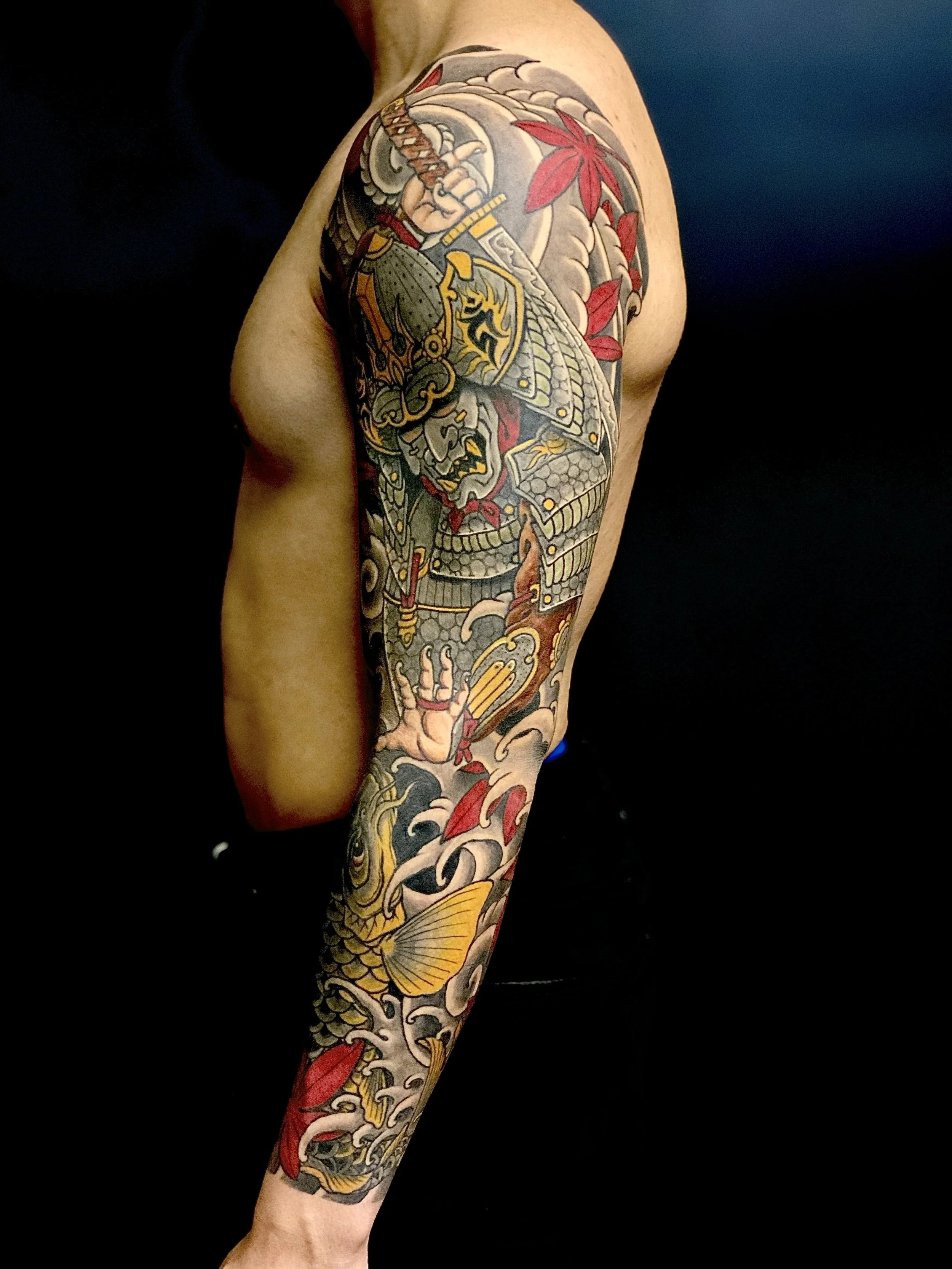 A person's full sleeve tattoo featuring a samurai warrior, a fierce dragon, koi fish, and red maple leaves in traditional Japanese style.