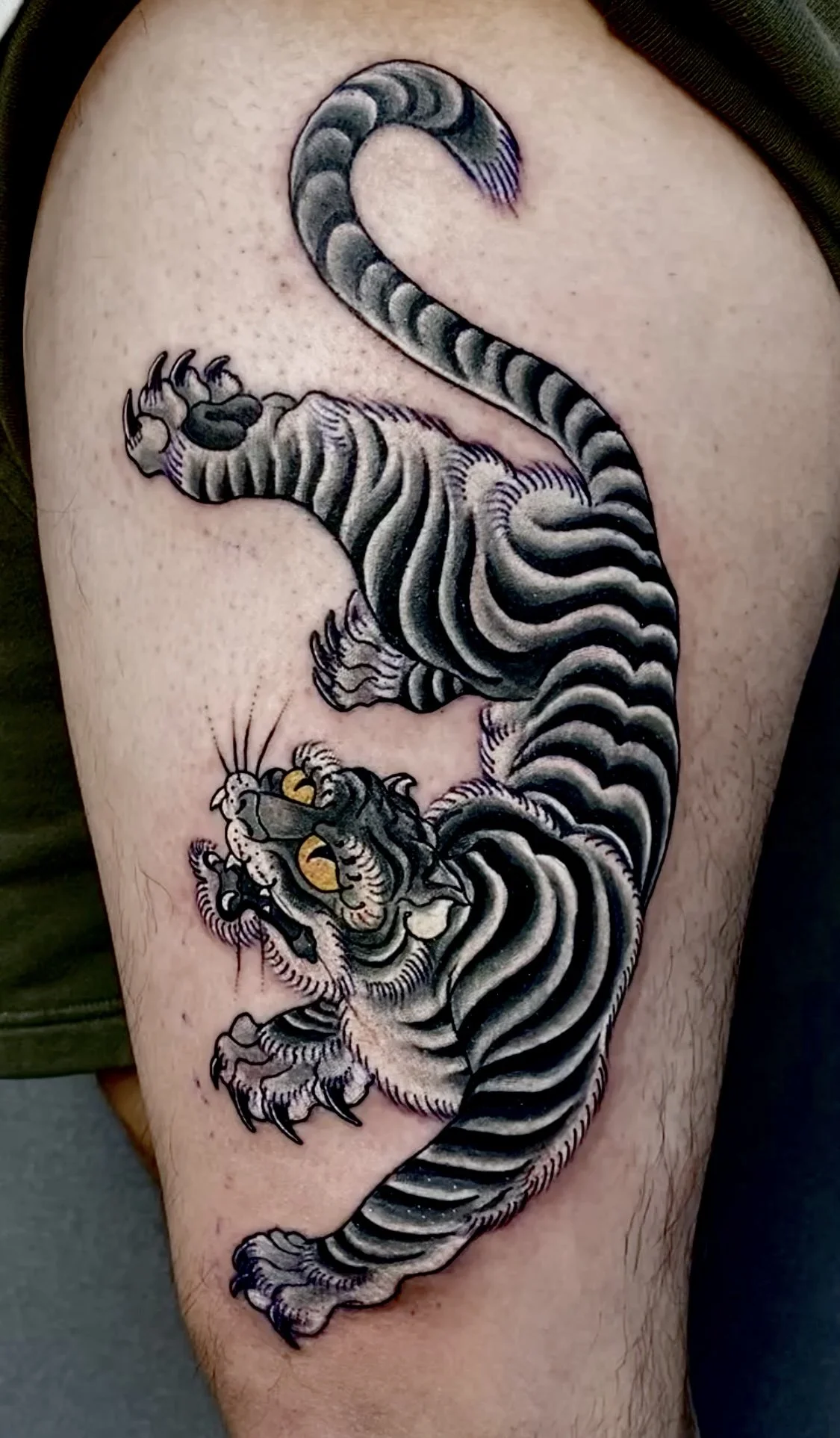 Black and gray tiger tattoo on person's upper arm with detailed stripes and fierce expression.