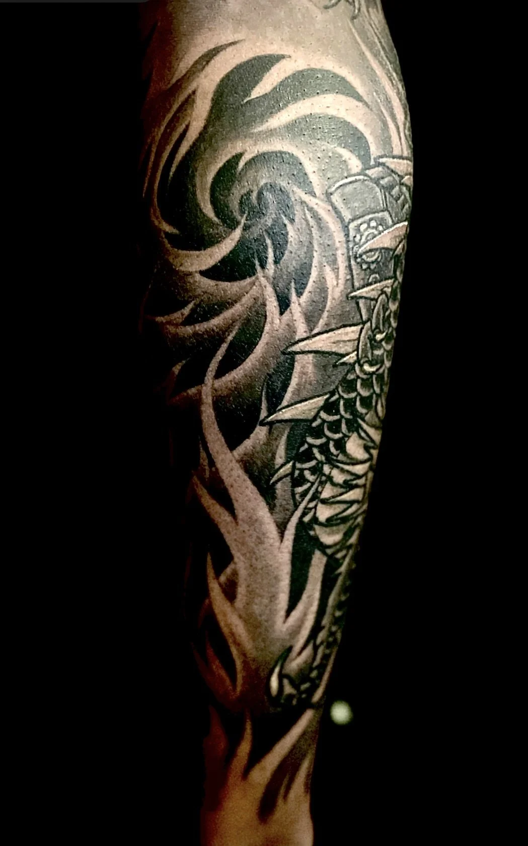 Close-up of a black and gray tattoo featuring a wave, flowers, and a boat on the arm.