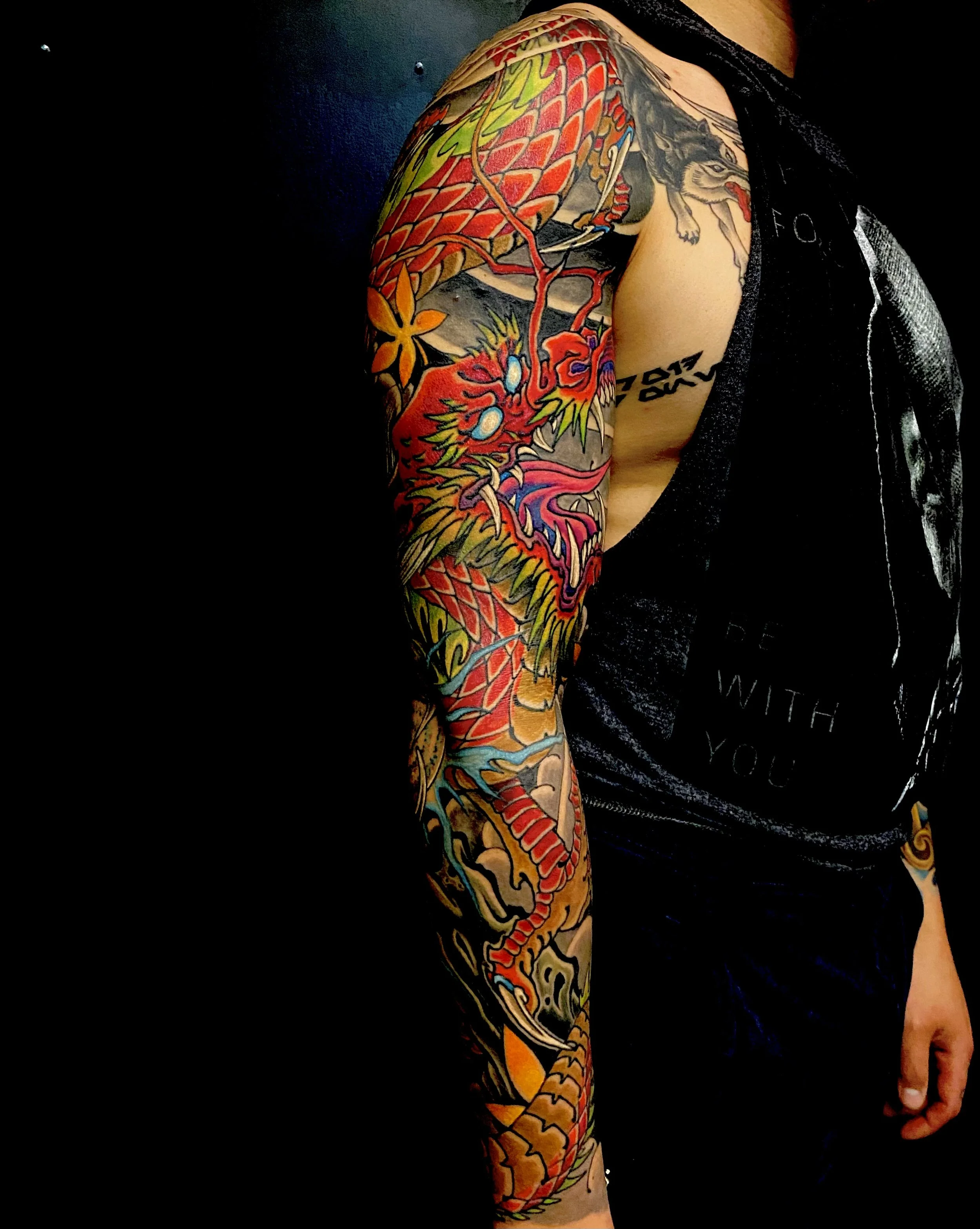 Colorful full sleeve tattoo of a dragon and a tiger on a person's arm against a dark background.