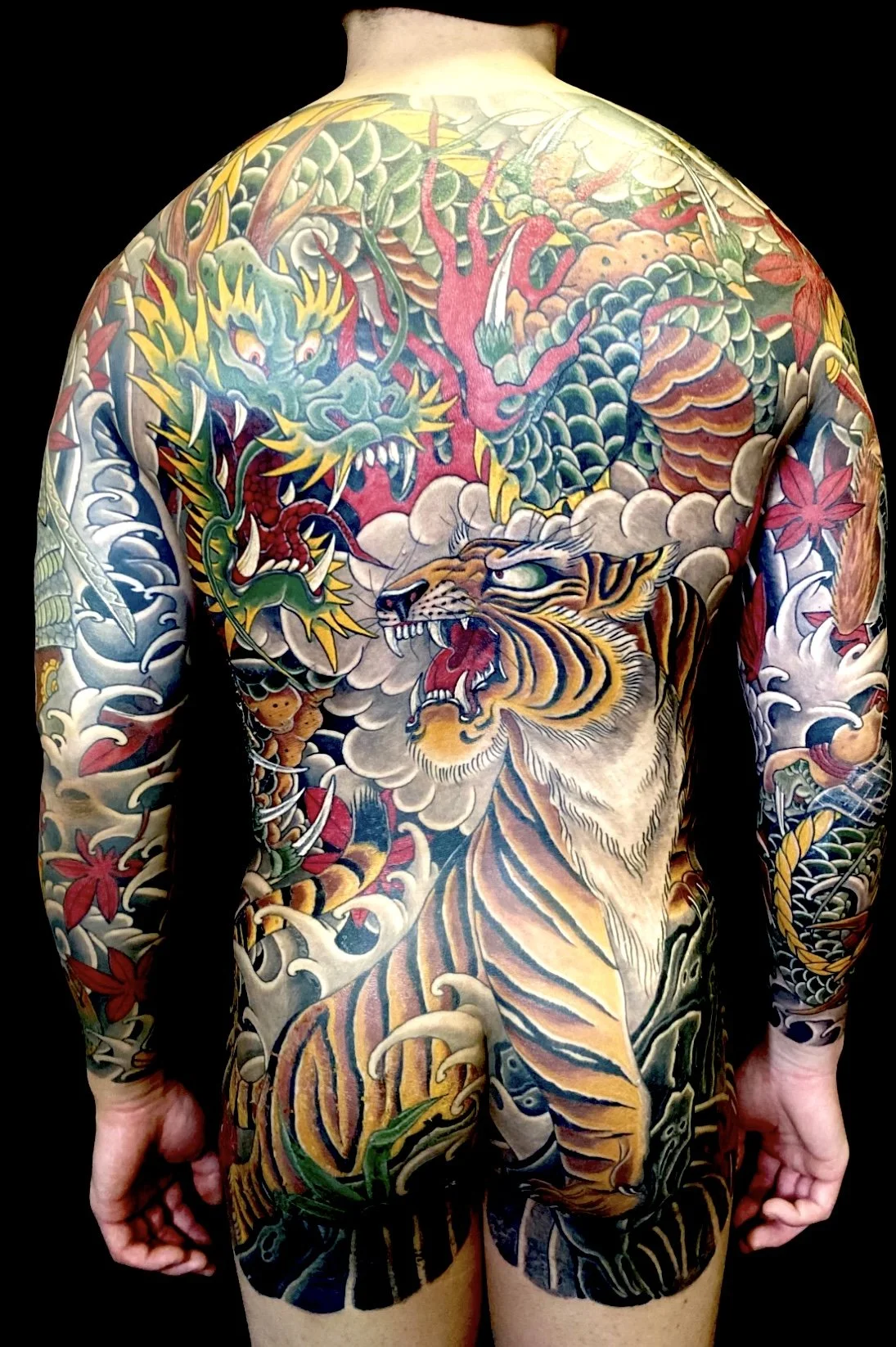 Colorful traditional Japanese-style tattoo of a tiger and a dragon on a person's back and arms.