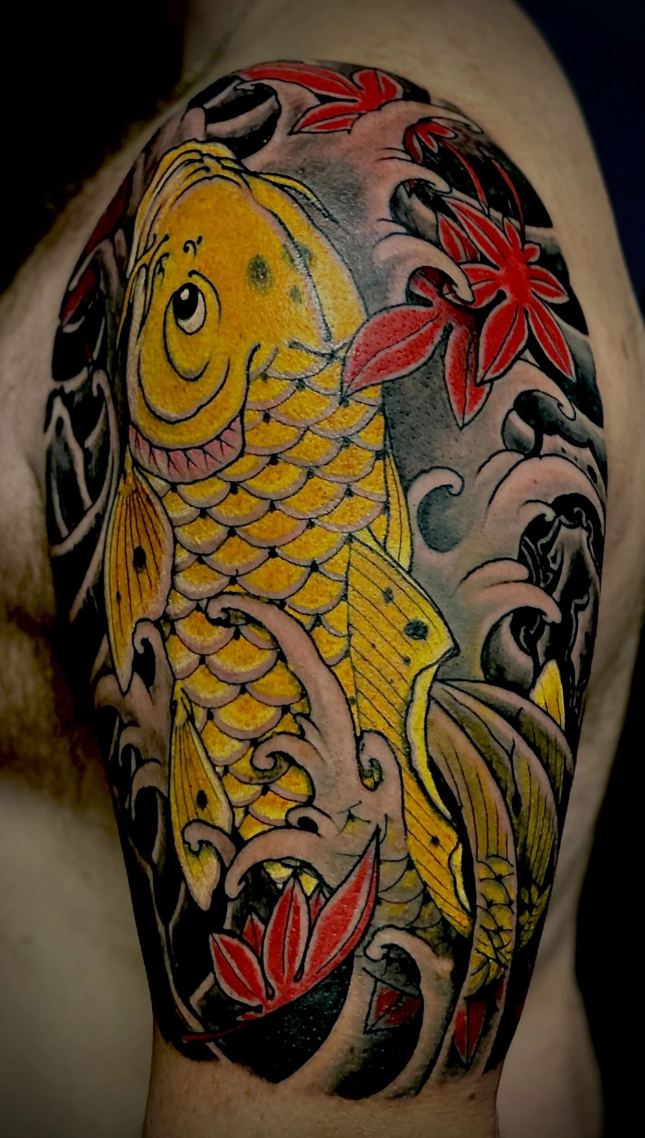 Tattoo of a yellow koi fish with red and black accents, surrounded by red maple leaves and black swirling waves.