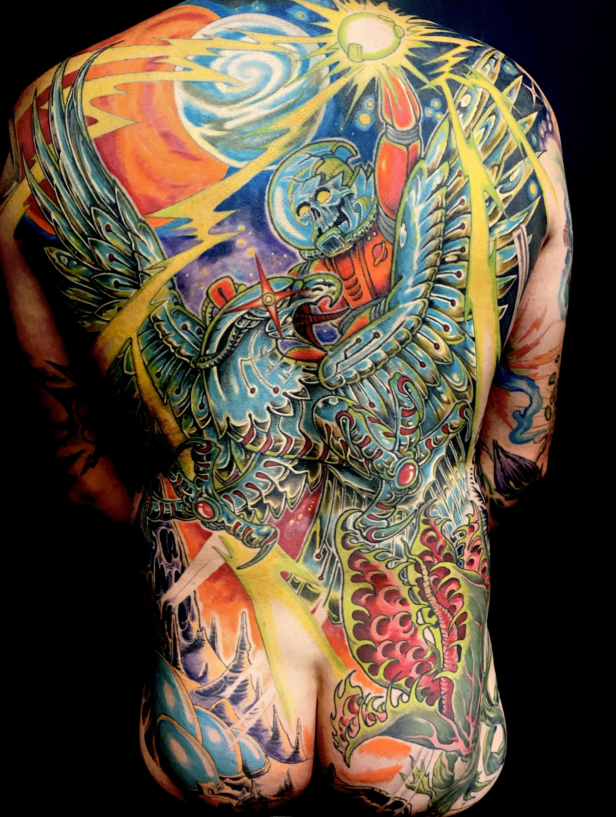 Colorful full-back tattoo featuring a mechanical eagle with skull elements, lightning bolts, and cosmic background with swirls, stars, and a bright sun.