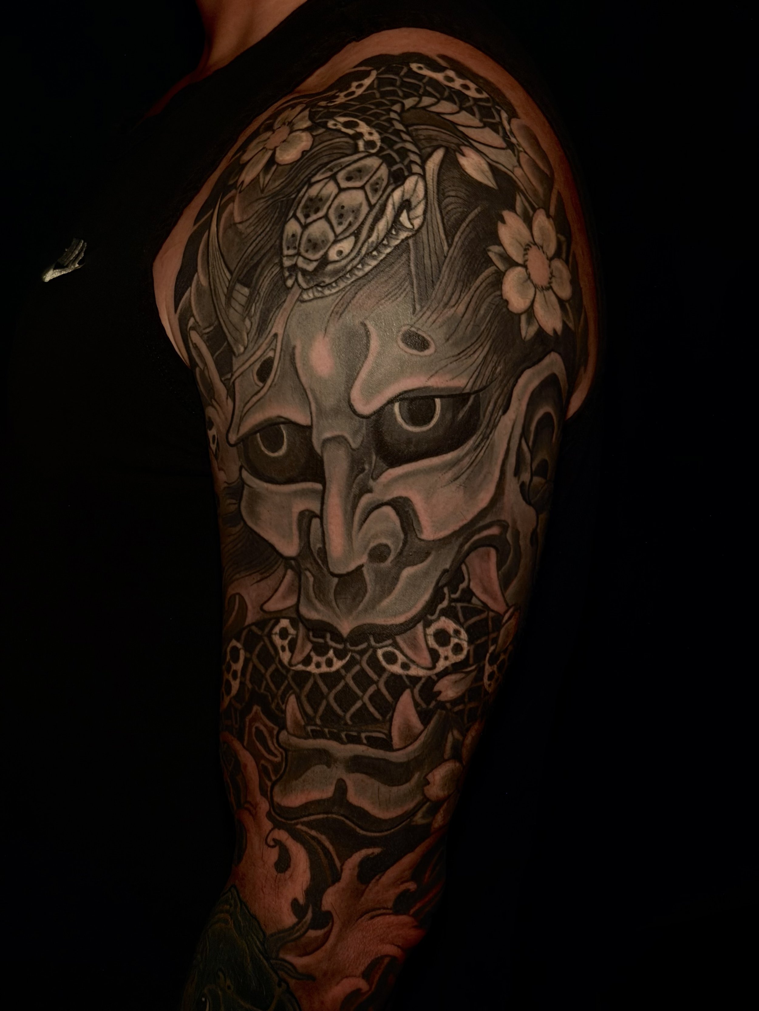 Tattoo on a person's arm featuring a snake’s head surrounded by flowers, with intricate line work and shading.