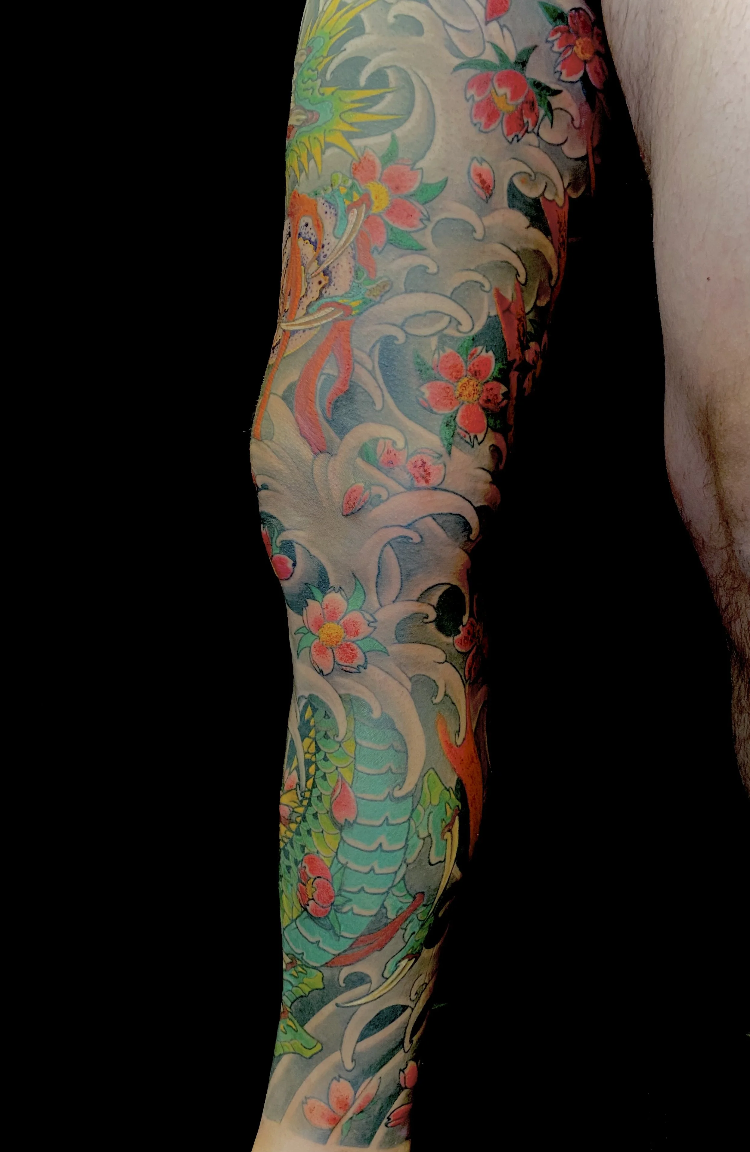 Colorful traditional Japanese-style tattoo of a dragon, cherry blossoms, and waves on a person's arm and chest.