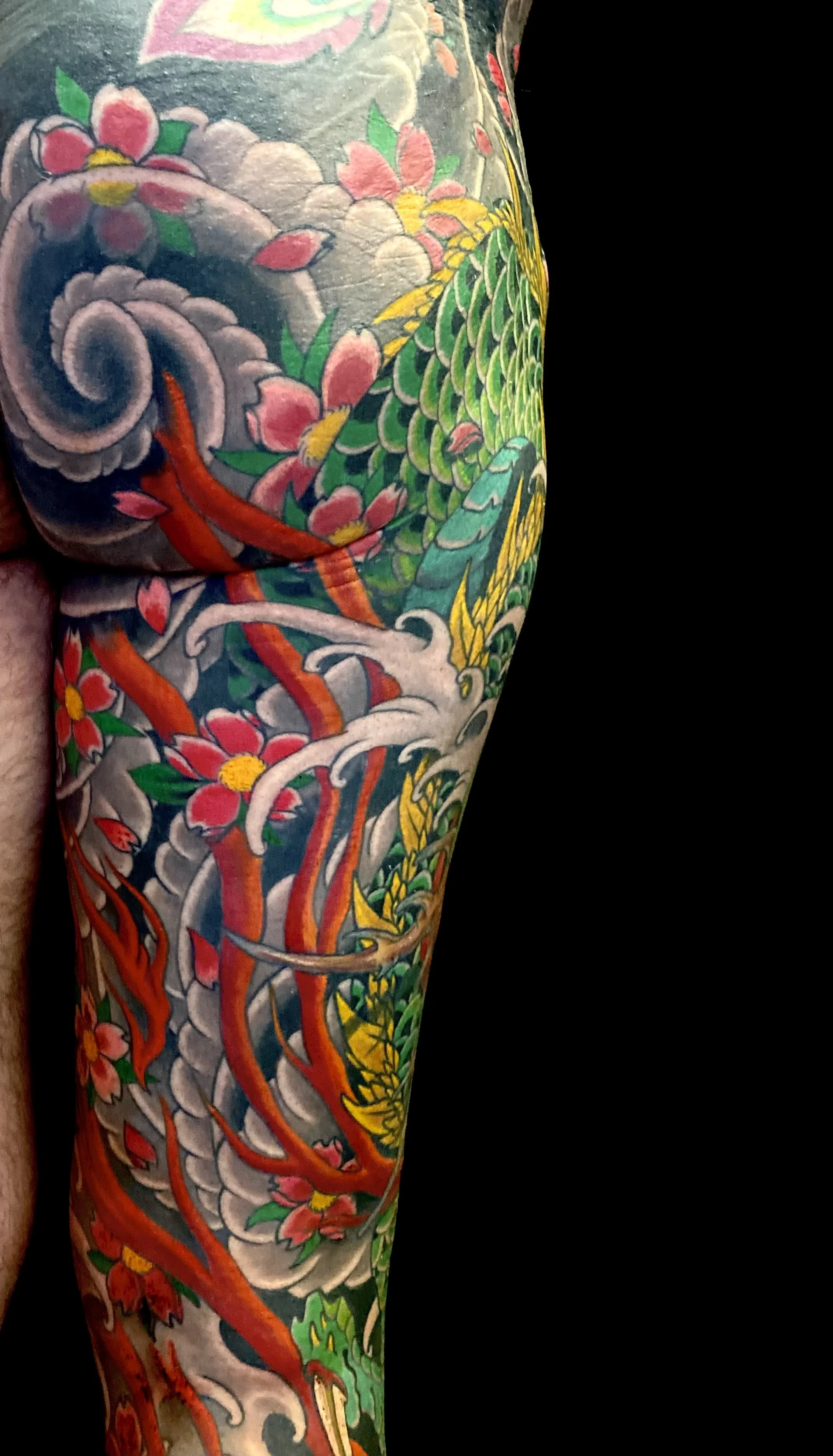 Colorful traditional Japanese style tattoo on arm, featuring a dragon, cherry blossoms, and swirling clouds.