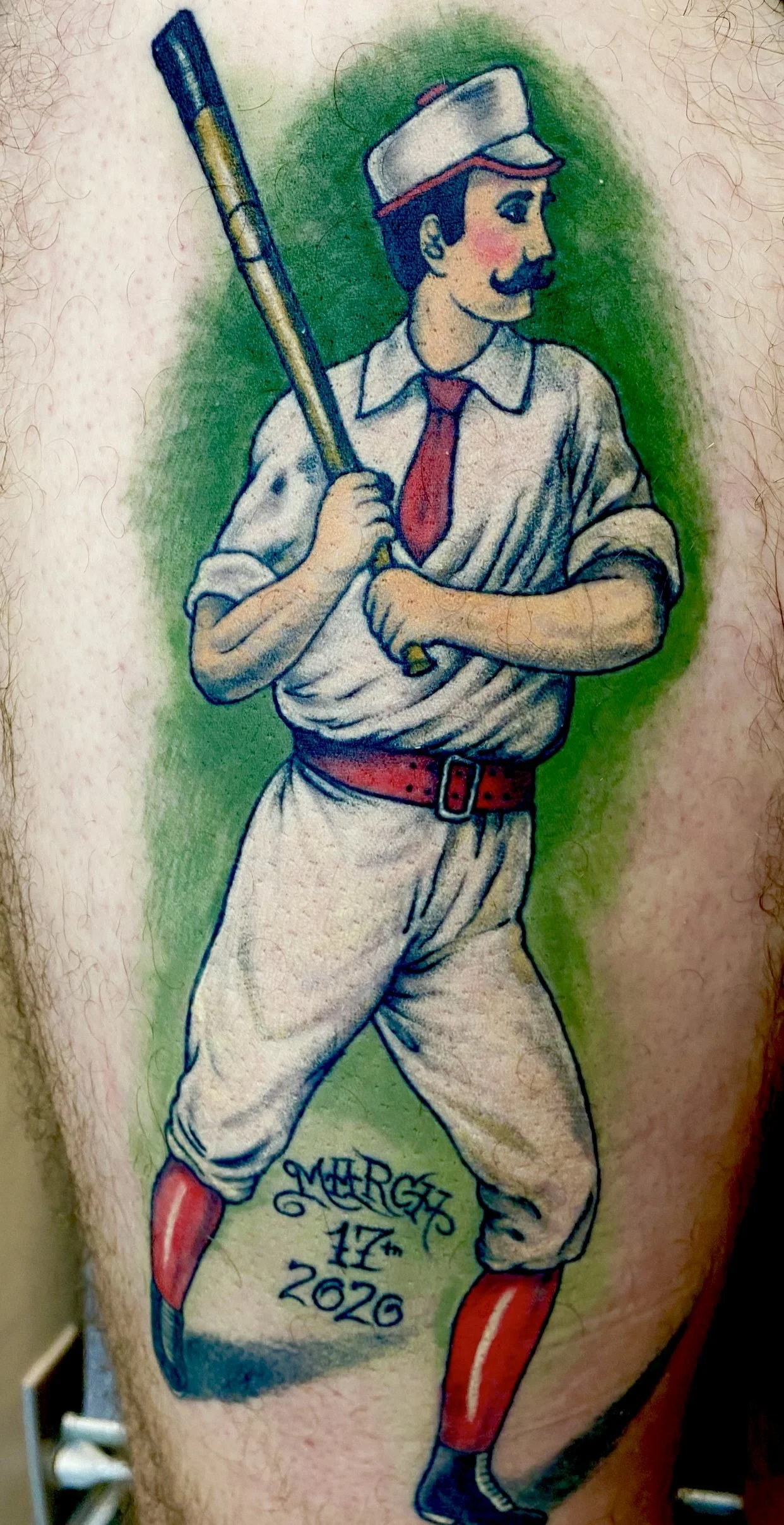 Tattoo of a man in vintage baseball uniform holding a bat, with signature and date 'March 17, 2026' on the leg.