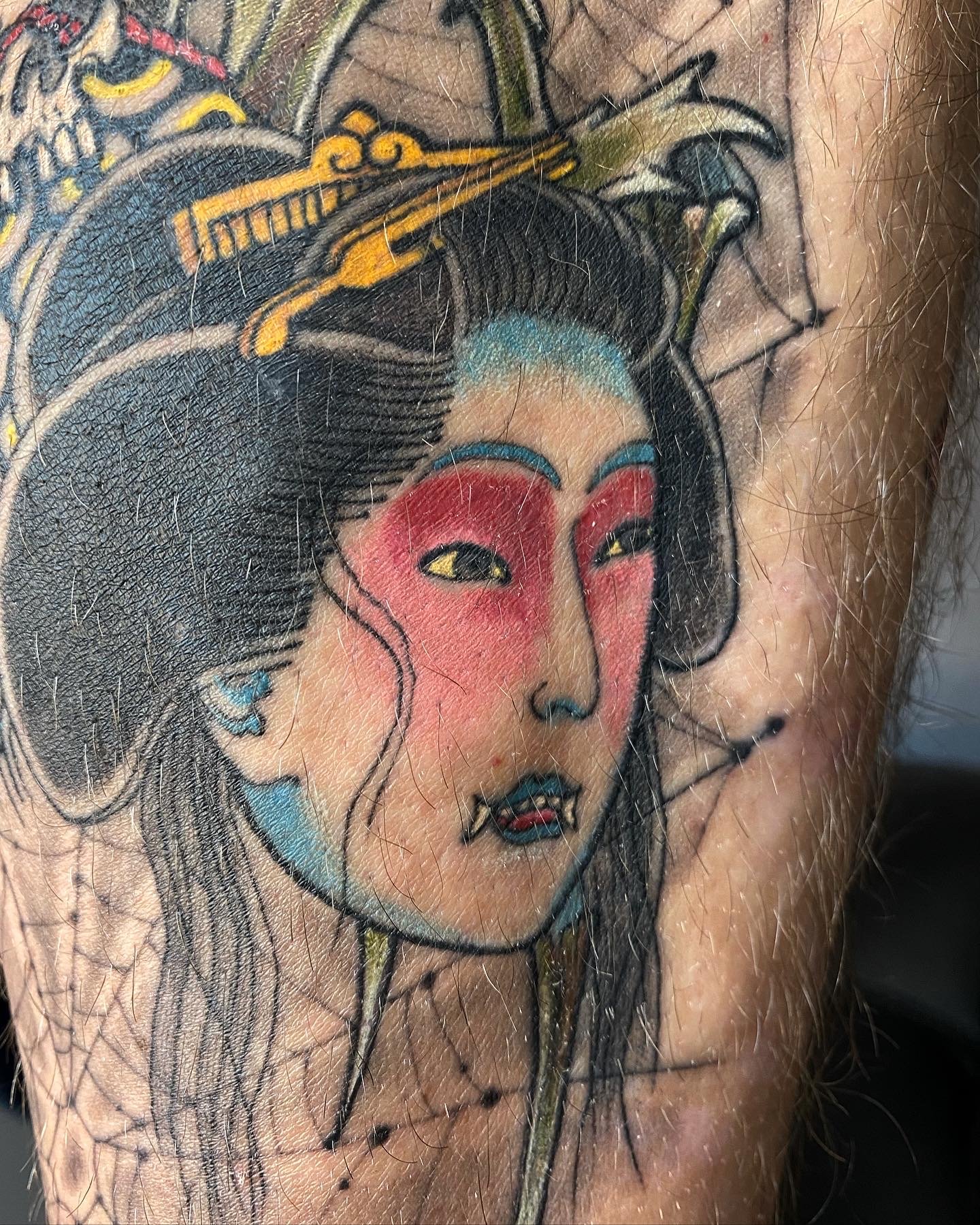 Colorful tattoo of a woman with traditional Japanese makeup and hairstyle, with red face paint and a Japanese hair ornament.