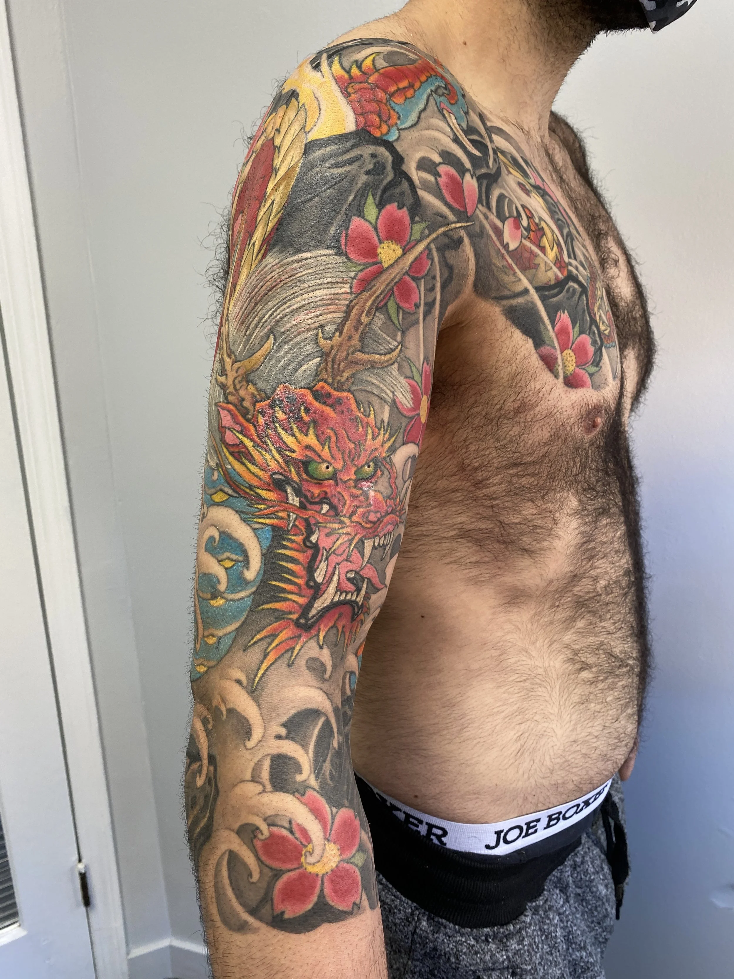 A man with a colorful traditional Japanese dragon and floral tattoo sleeve on his left arm.