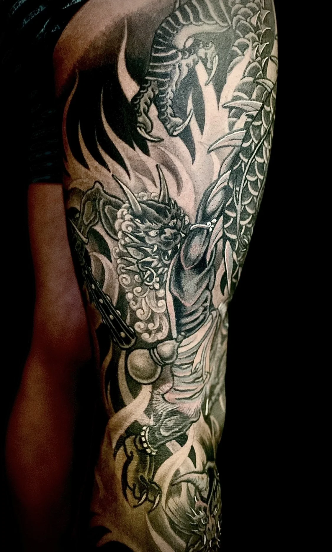 Black and gray tattoo on person's arm featuring a dragon and a tiger amidst leafy branches.