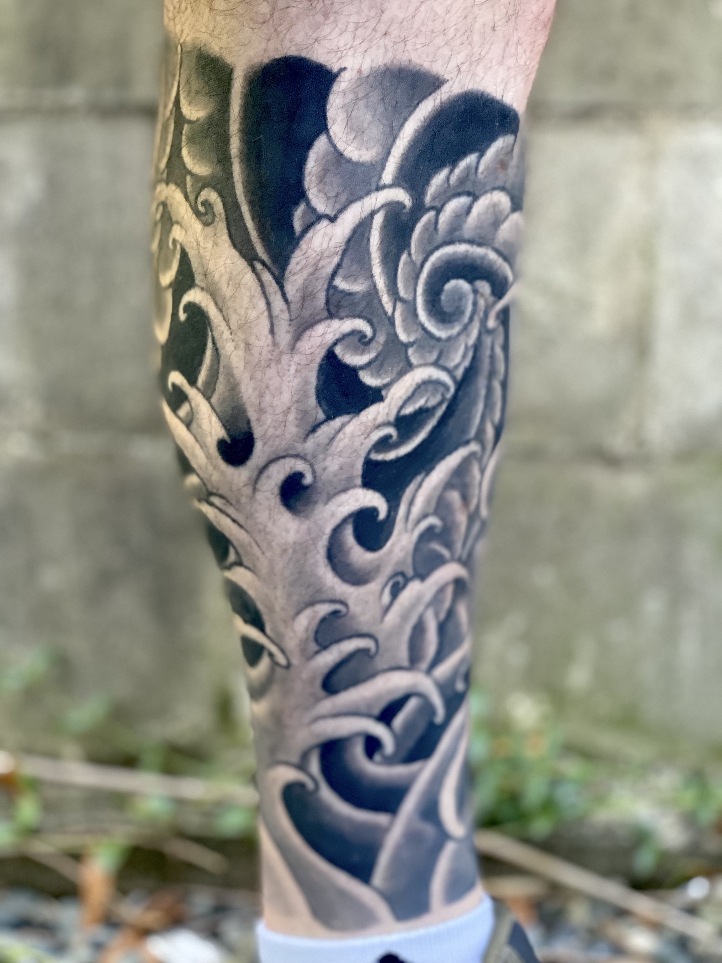 Tattoo sleeve on a person's arm featuring stylized waves in black and gray ink.