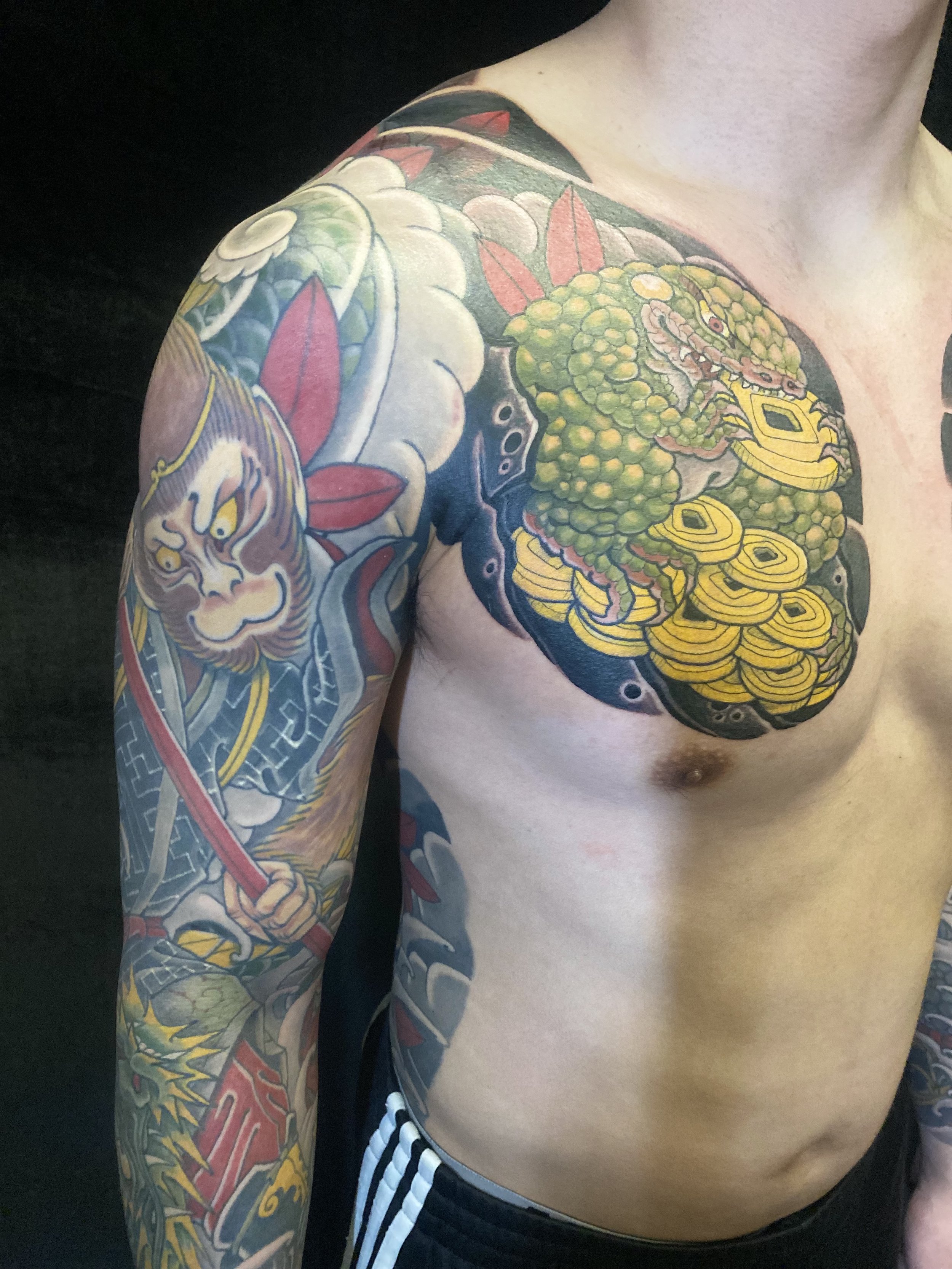 Colorful traditional Japanese tattoo on a man's chest and arm, featuring a fierce lion, a mythological creature, clouds, and floral elements.