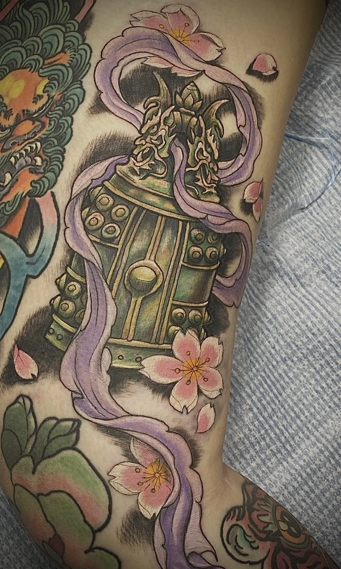 Colorful tattoo of a green and gold armored warrior with cherry blossom flowers and purple ribbons on arm