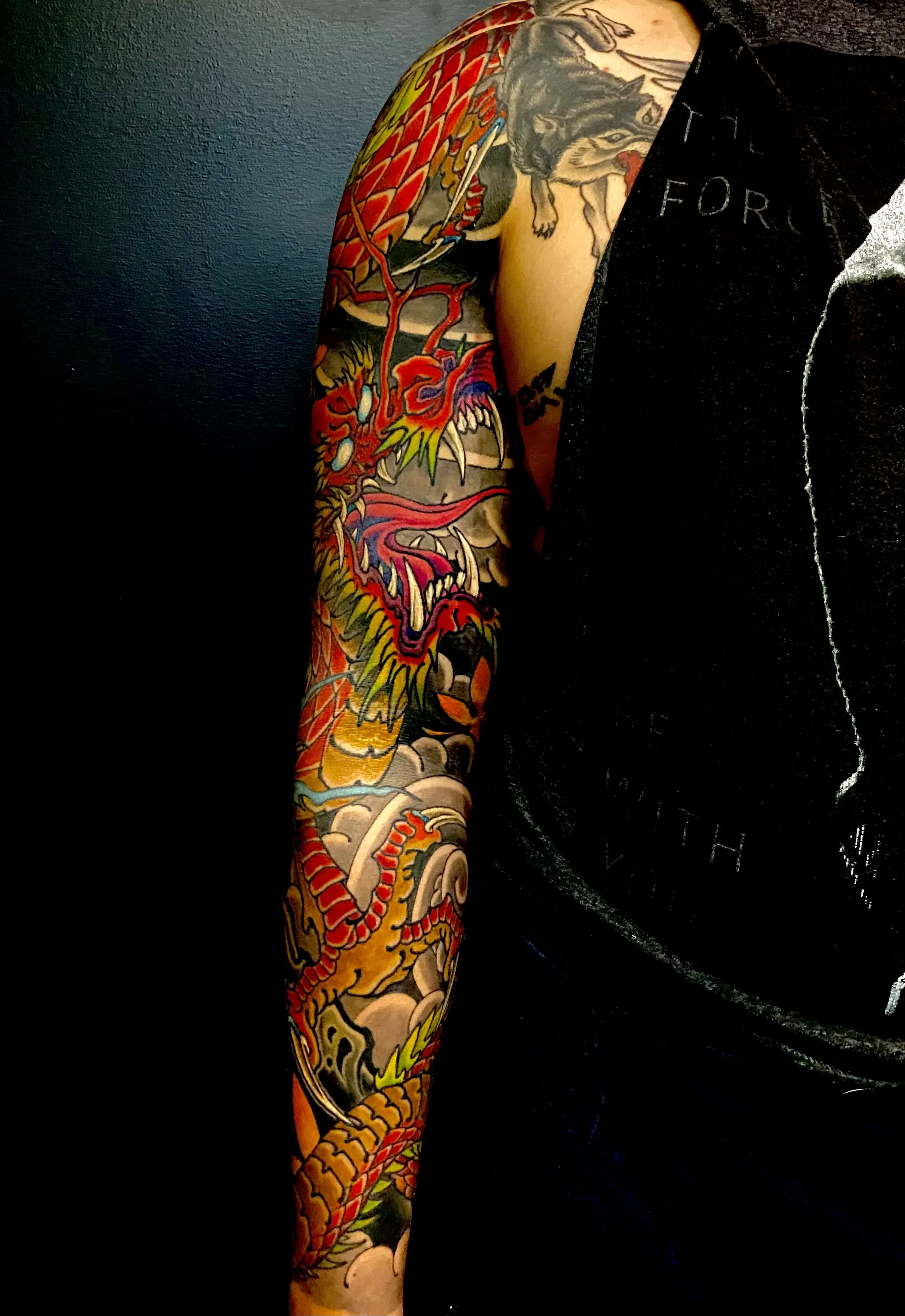 Colorful Japanese-style dragon tattoo on a person's arm, featuring a fierce dragon with red, yellow, and green accents.
