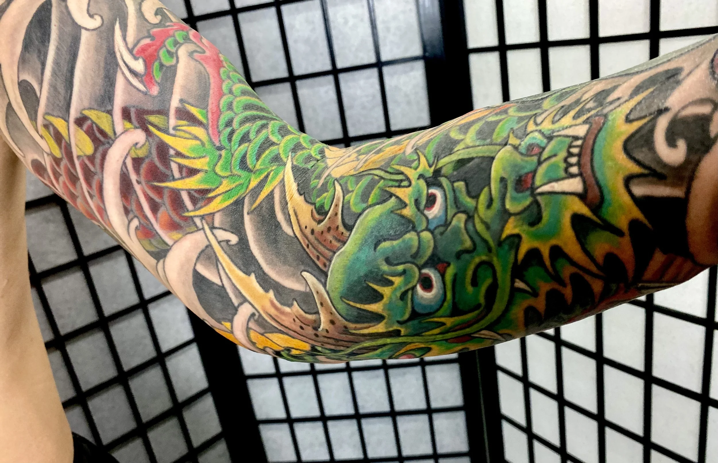 Colorful tattoo of a green dragon on an arm, set against a black grid background.