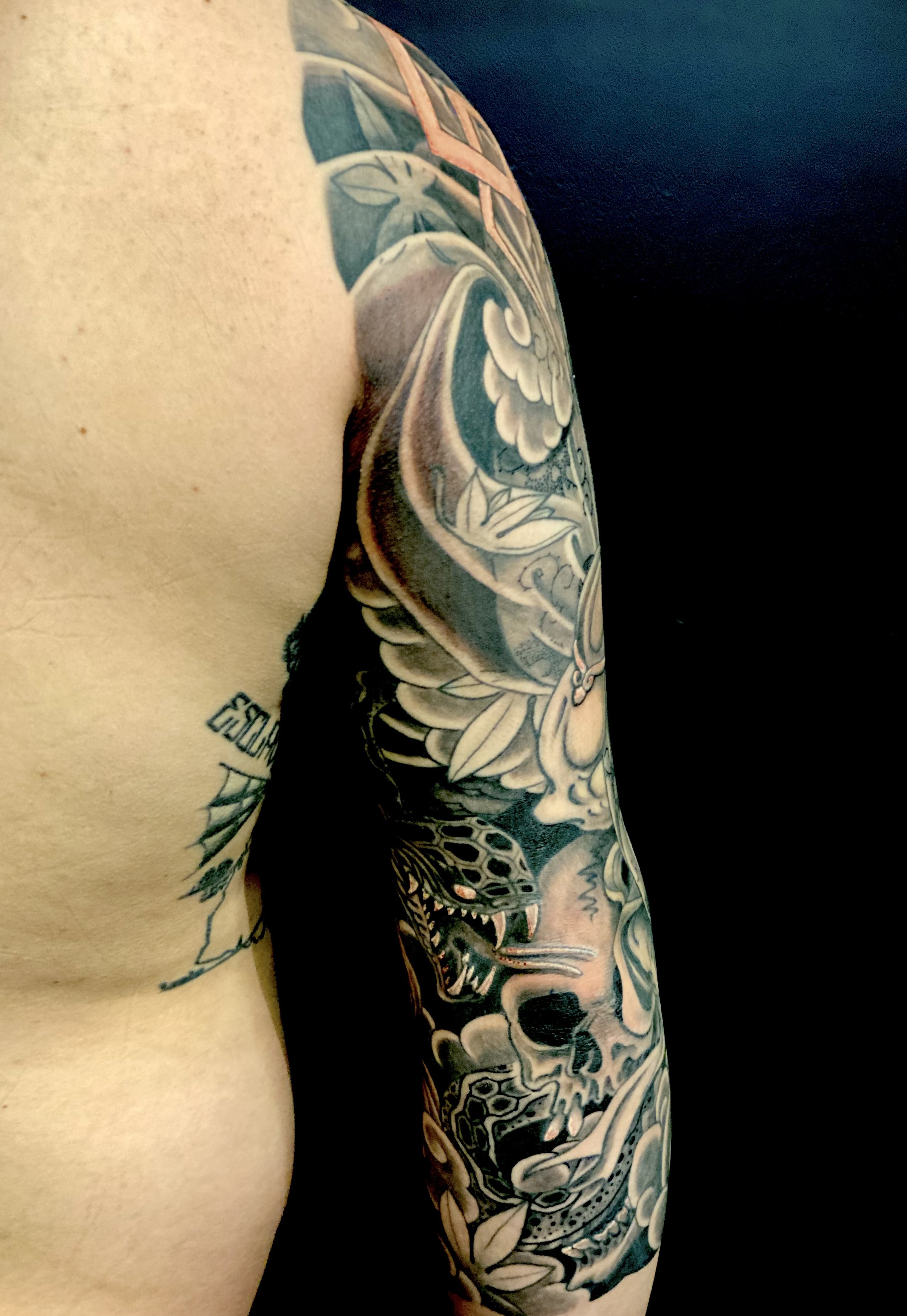 Tattoo sleeve featuring a dragon, skull, flowers, and other detailed elements on a person's arm.